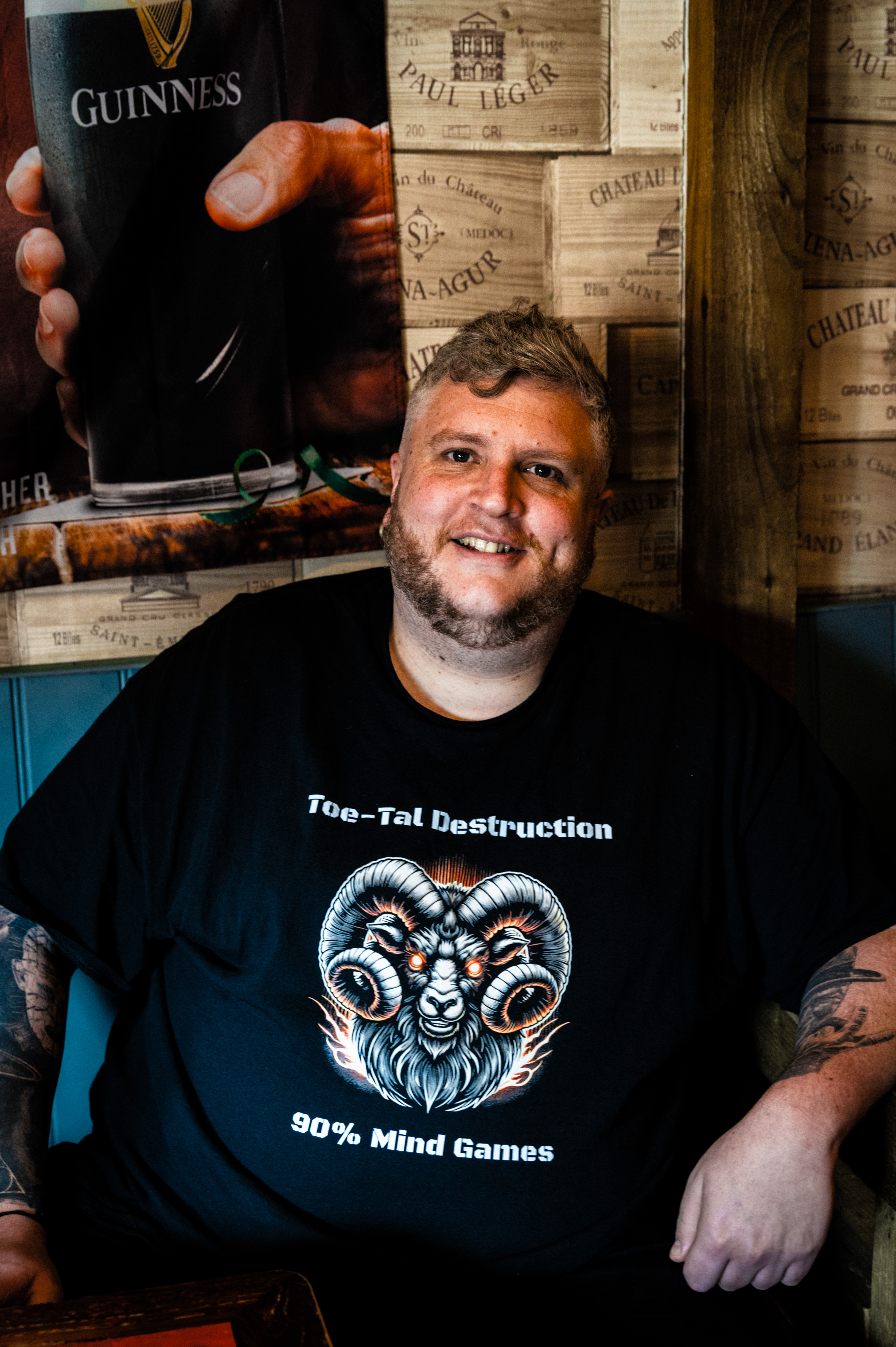 A smiling man wearing a black t-shirt with a graphic design of a ram's head and the text "Toe-tal Destruction 90% Mind Games".