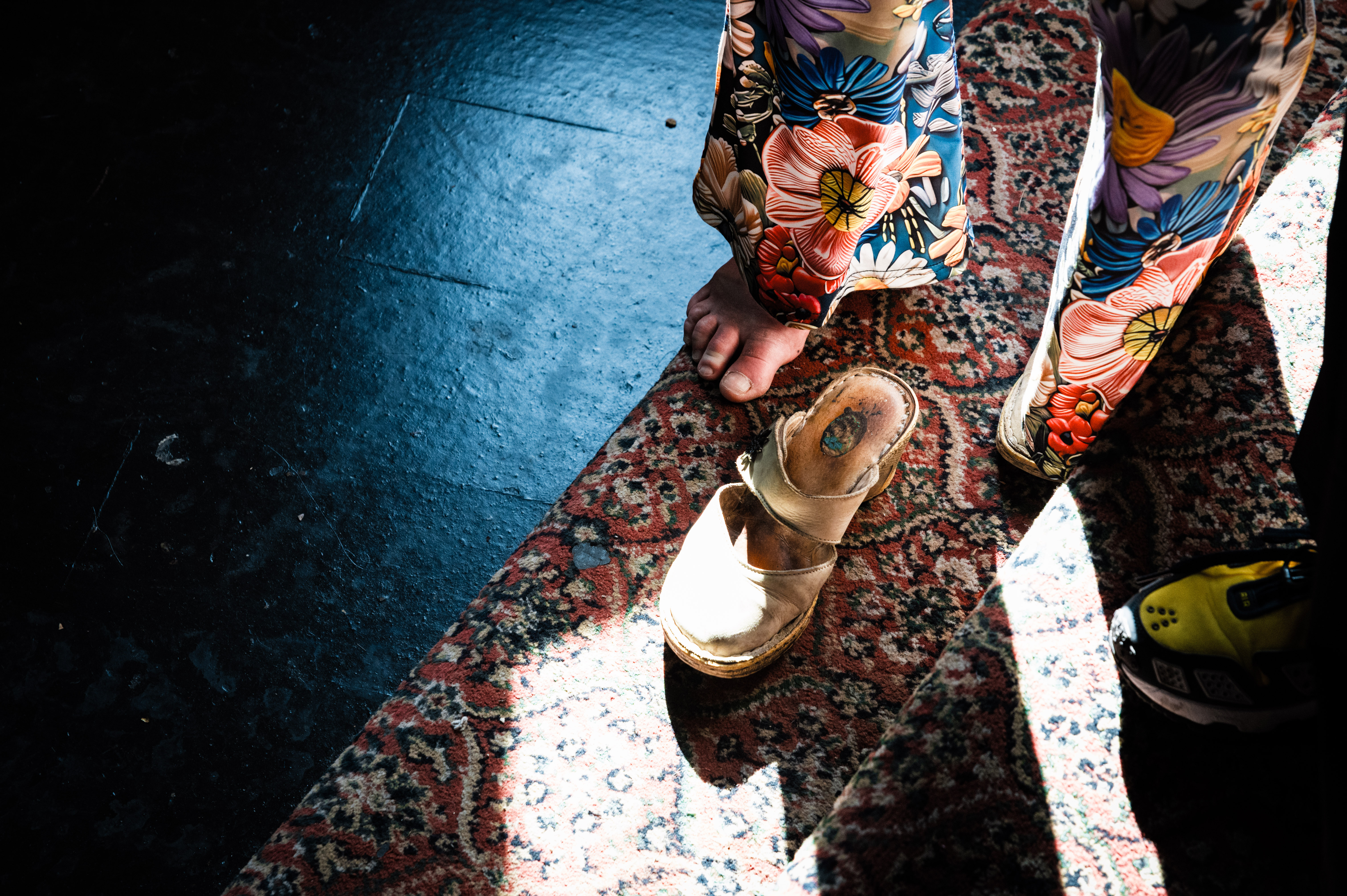Floral-patterned trousers, feet in gold sandals on patterned rug.