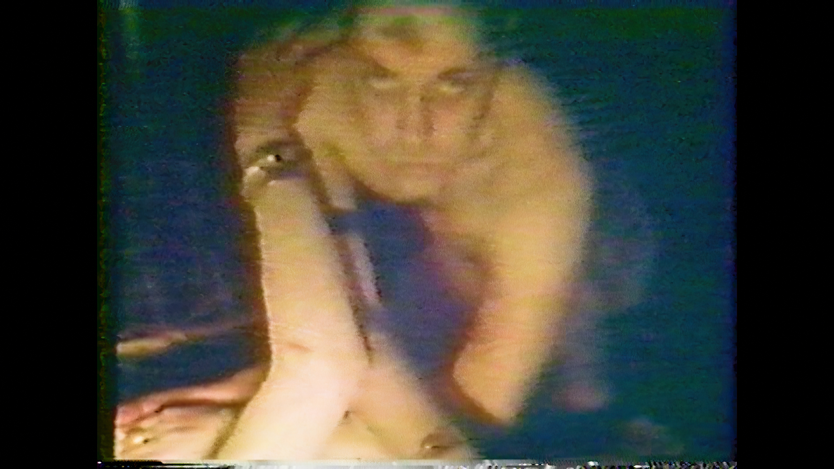 Blurry, low-quality image showing a person with blonde hair in purple clothing, hand positioned near face against dark background.