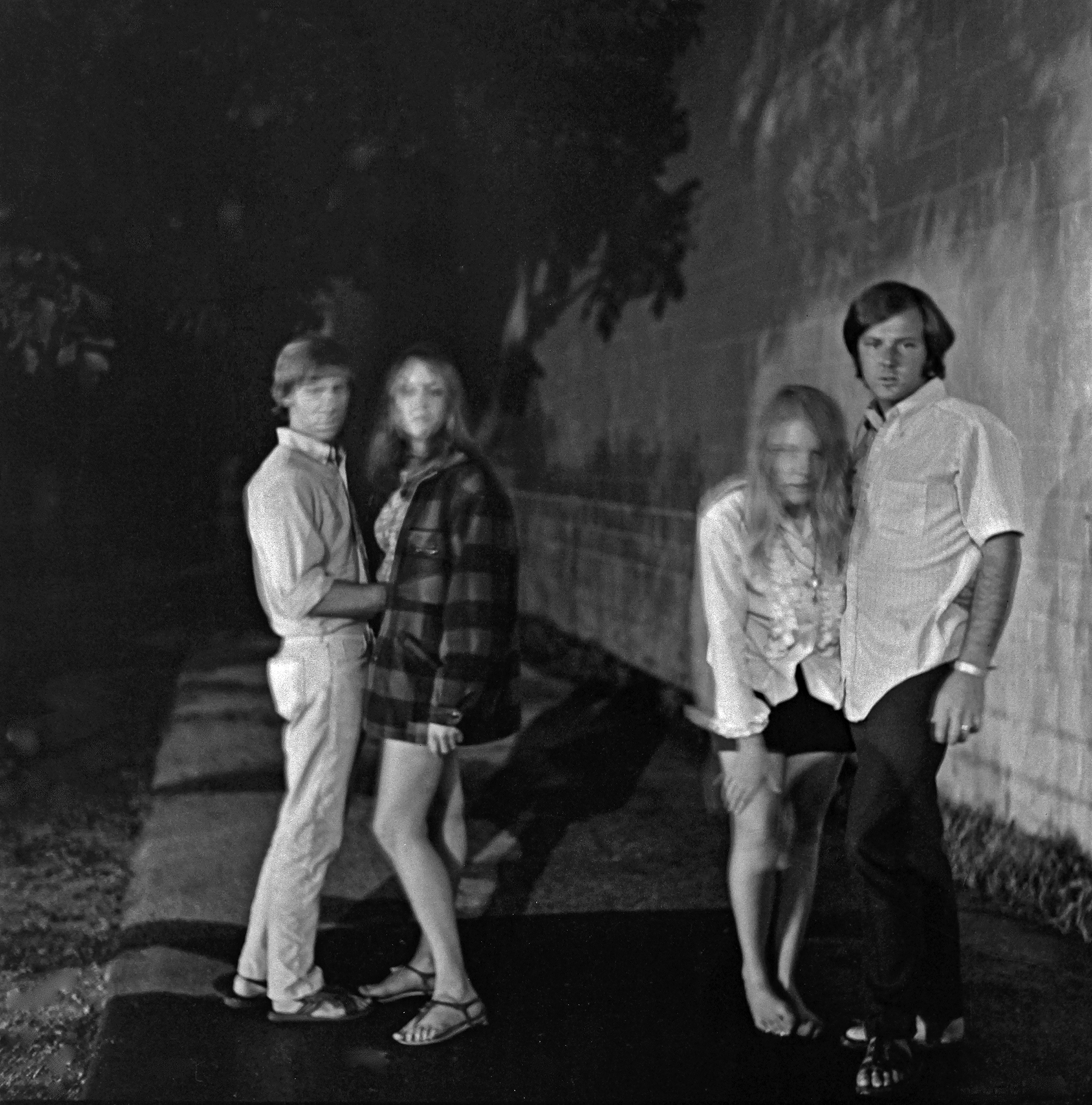 Four young people, two men and two women, posing outdoors at night.
