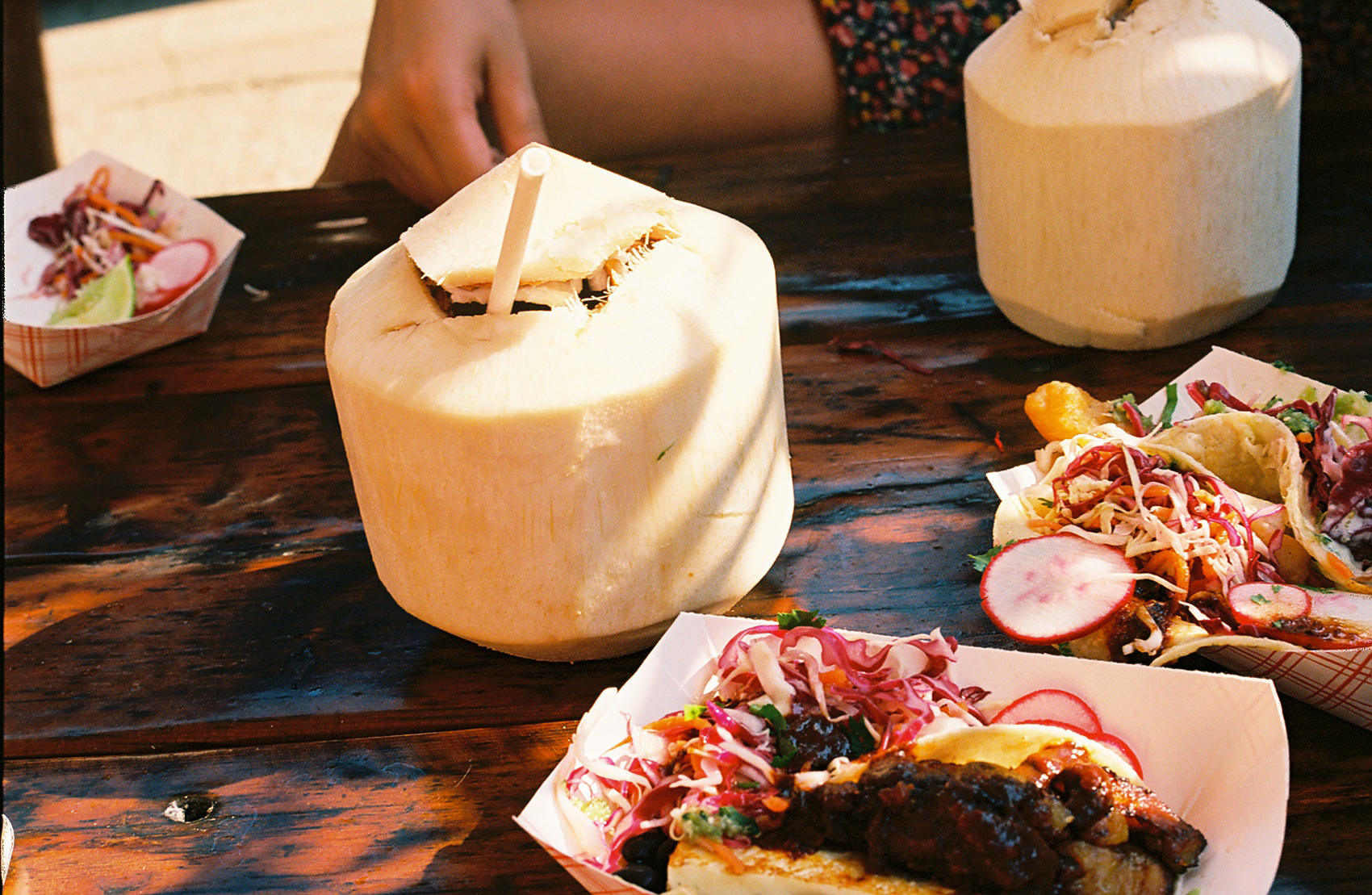 Wooden board with open coconut, sliced cold cuts, bread and salad.