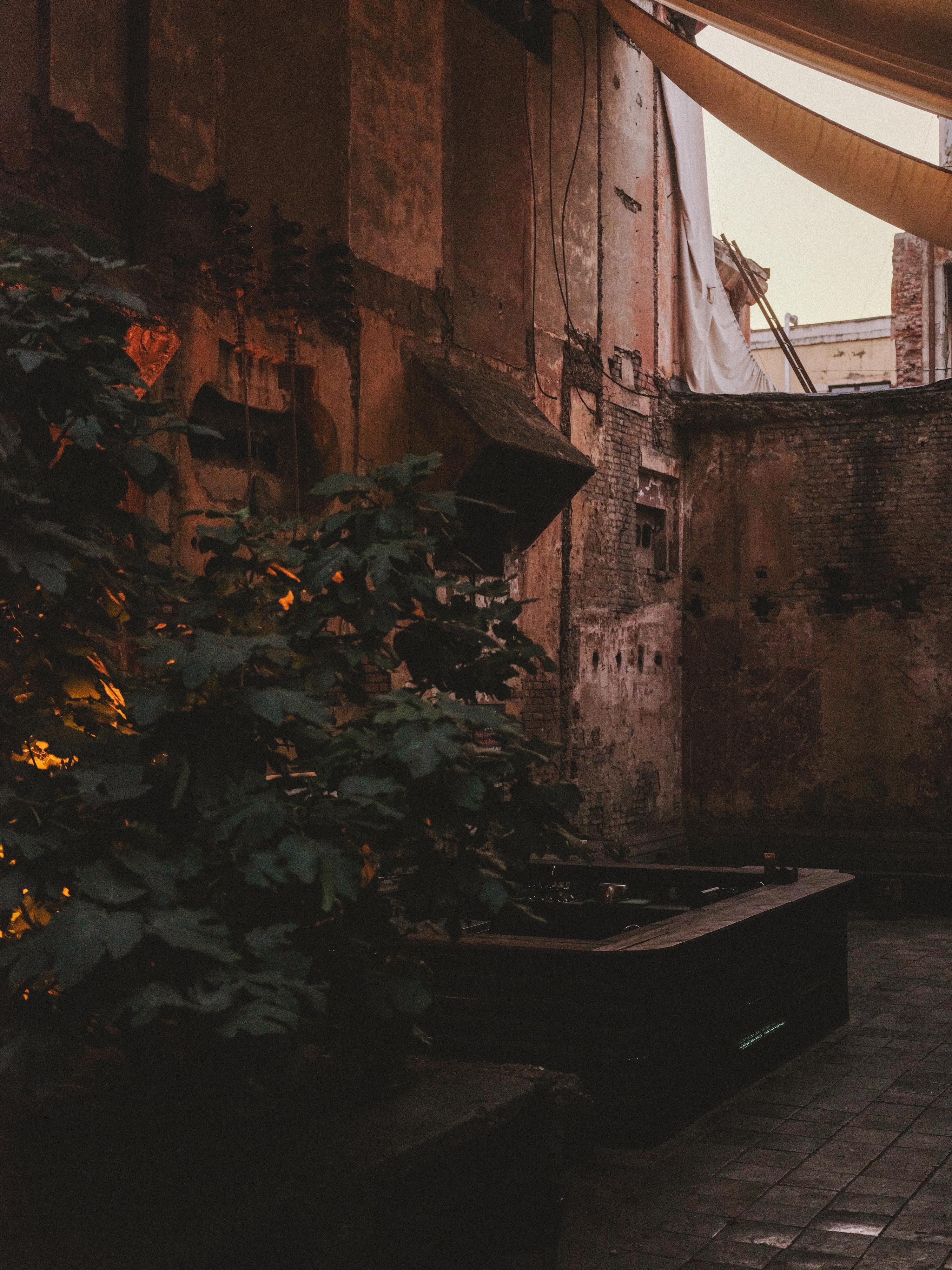 Digital illustration of narrow courtyard with brown brick walls, green foliage, washing lines with white fabric, warm orange lighting.