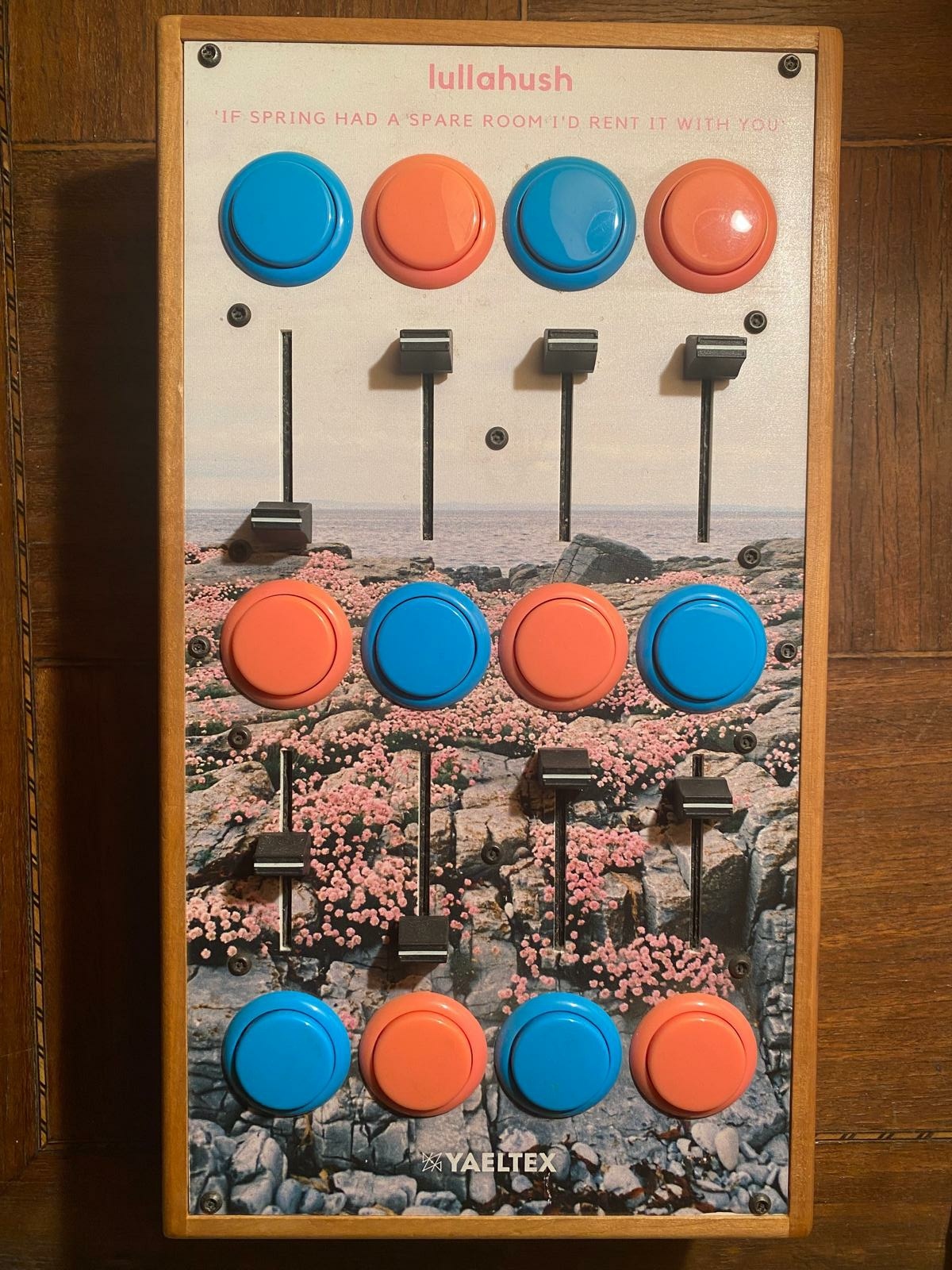 Control panel with 4 large blue and orange buttons, 3 smaller black buttons, and a background image of a field of pink flowers.