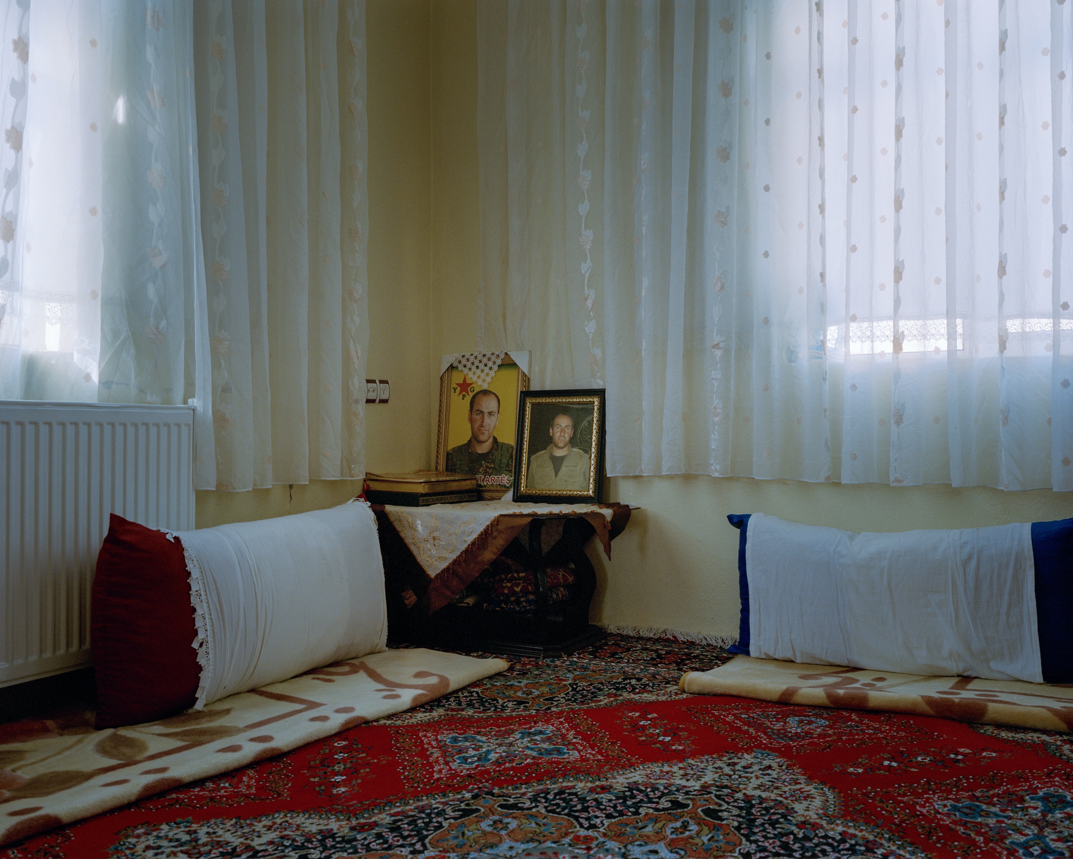 Ornate rug covering floor; decorative furniture; framed portraits on shelves; curtains draped across window.