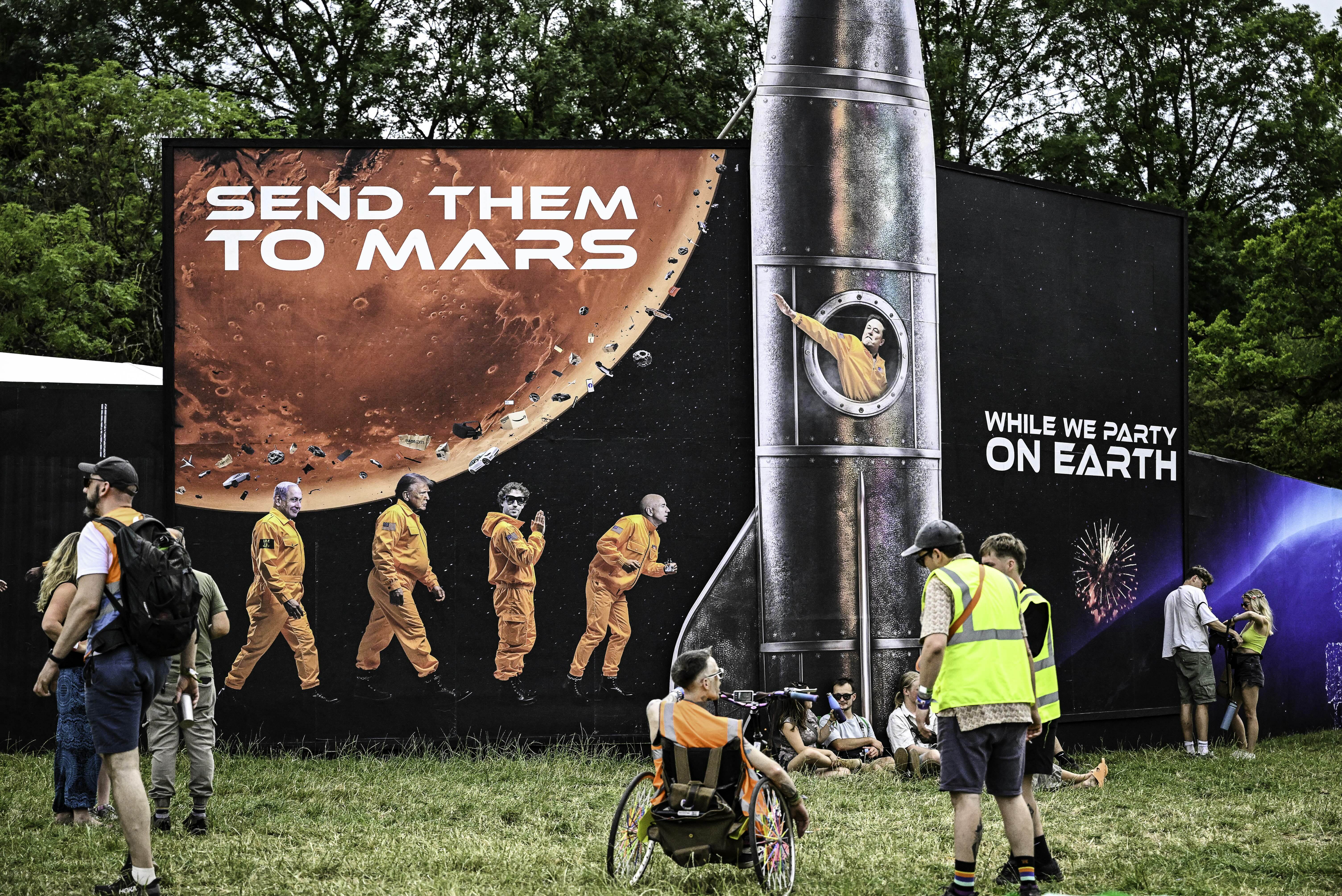 Large outdoor mural showing red Mars planet, astronaut figures, and silver rocket with "SEND THEM TO MARS" text. High-vis workers nearby.