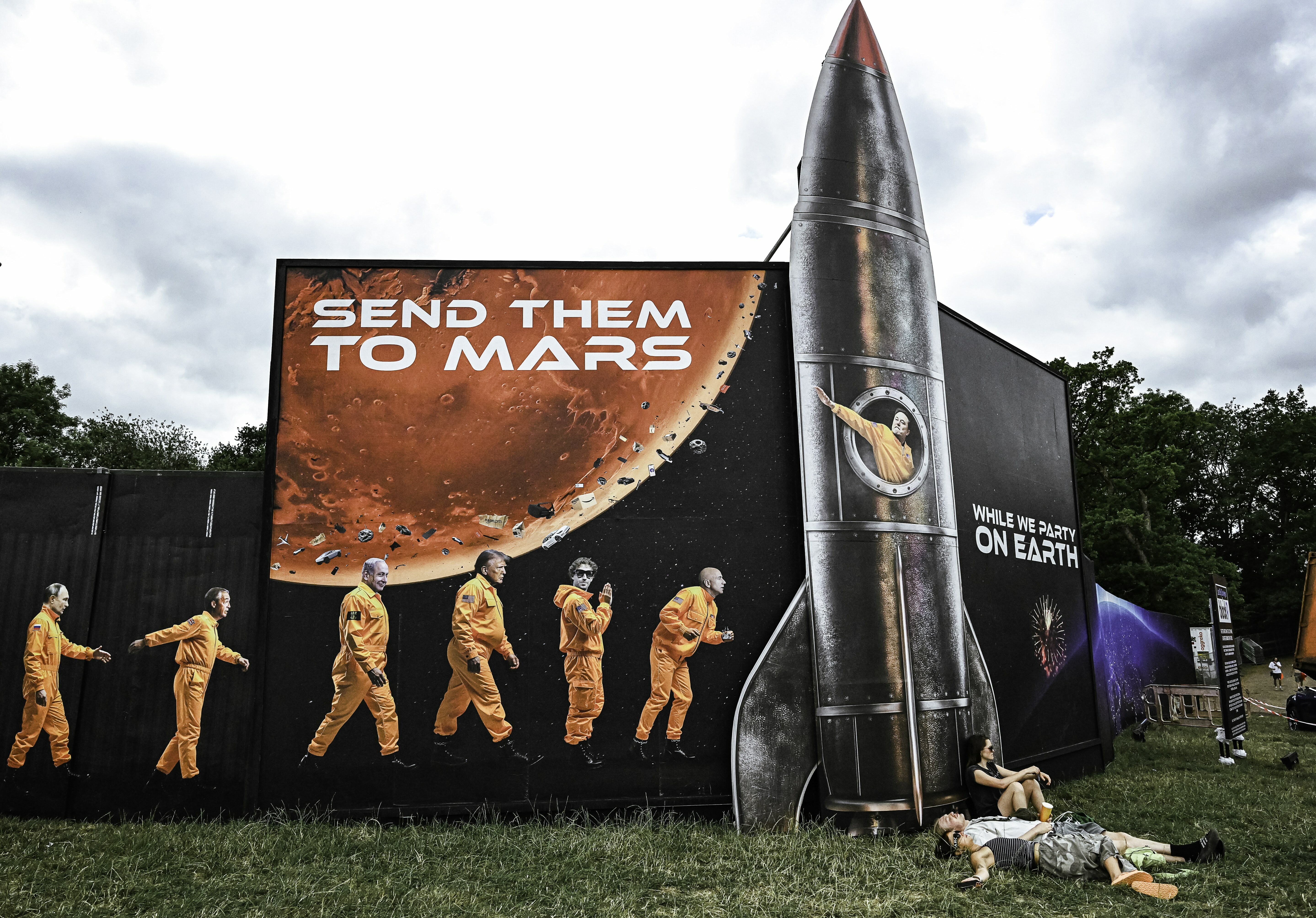 Street mural with red Mars planet, text "SEND THEM TO MARS", orange-suited figures walking, and grey rocket structure beside it.