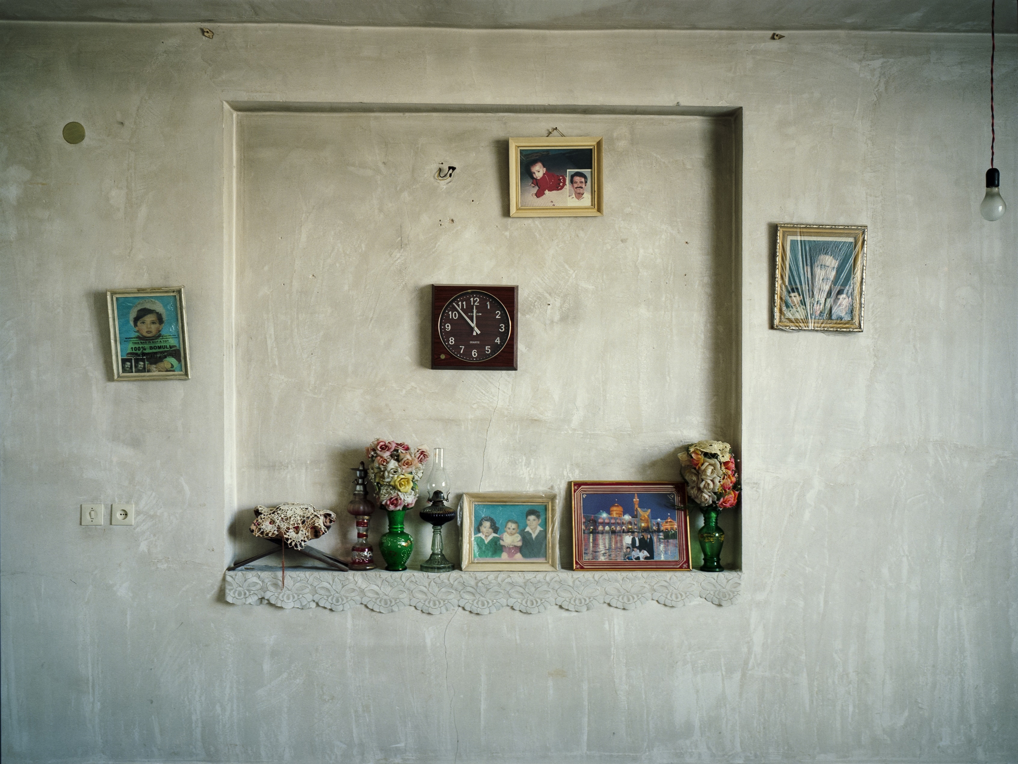 Shelving unit against wall with various framed illustrations, vases with flowers, and a clock.