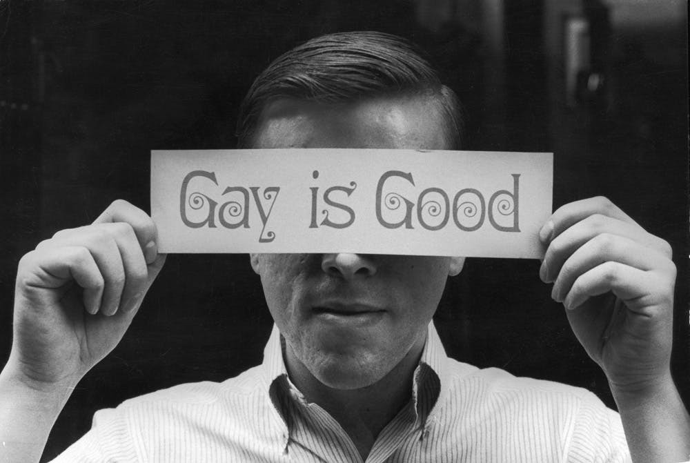 A man holding a sign that says "Gay is Good" in front of his face.