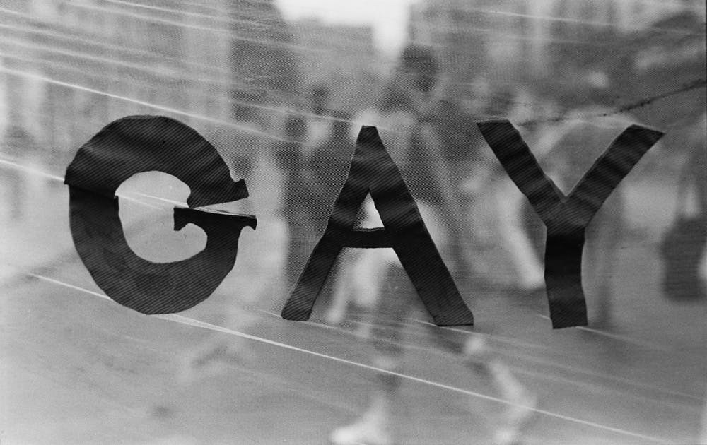 Black capital letters spelling "GAY" on a blurred background.