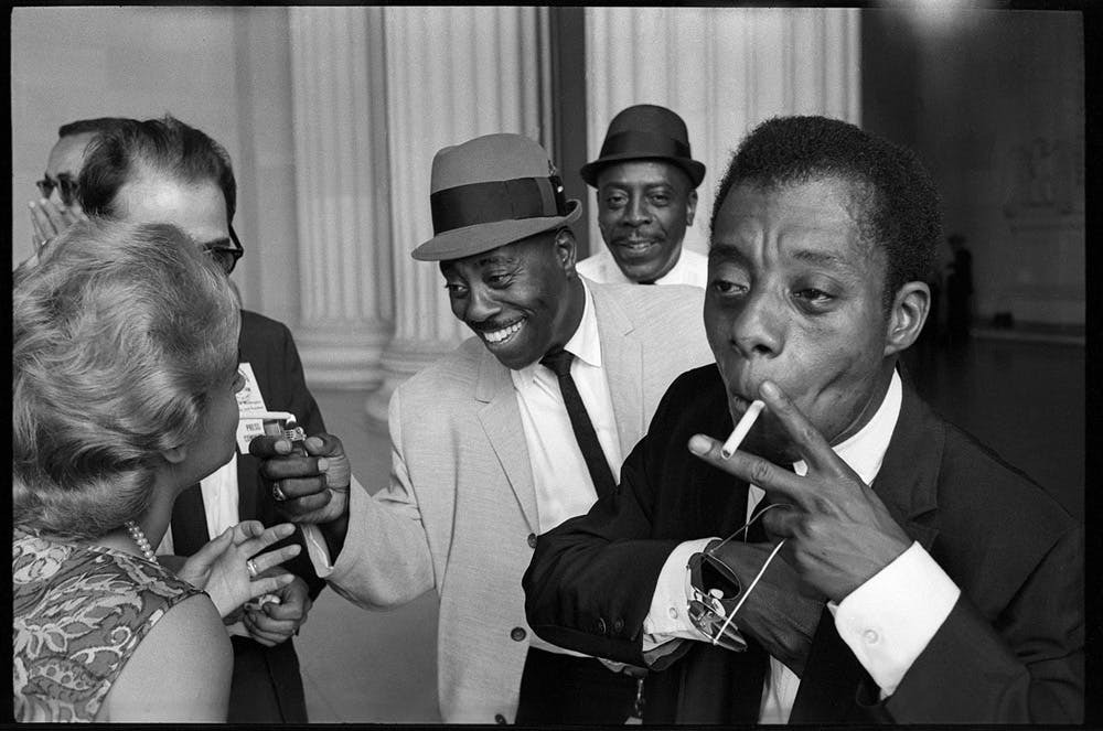 Group of men in suits, one smoking a cigarette, in a formal setting.