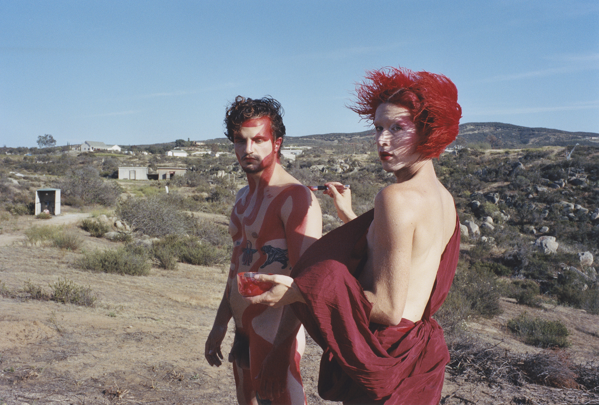 Two individuals, a man and a woman, wearing vibrant red outfits against a desert landscape.