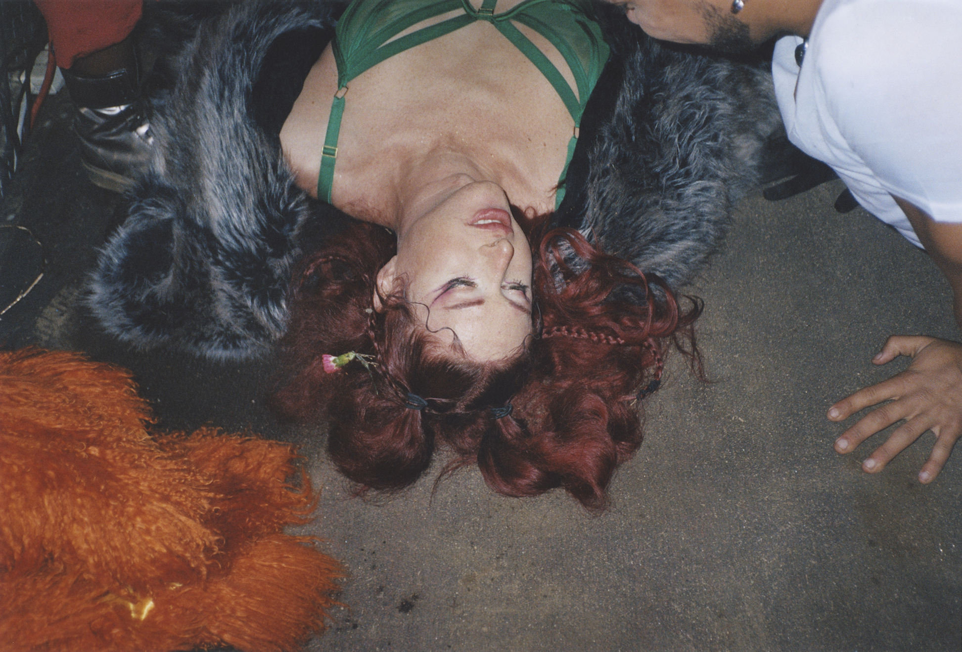 Image of a person with curly red hair lying on the ground, surrounded by colourful fabrics and decorations.