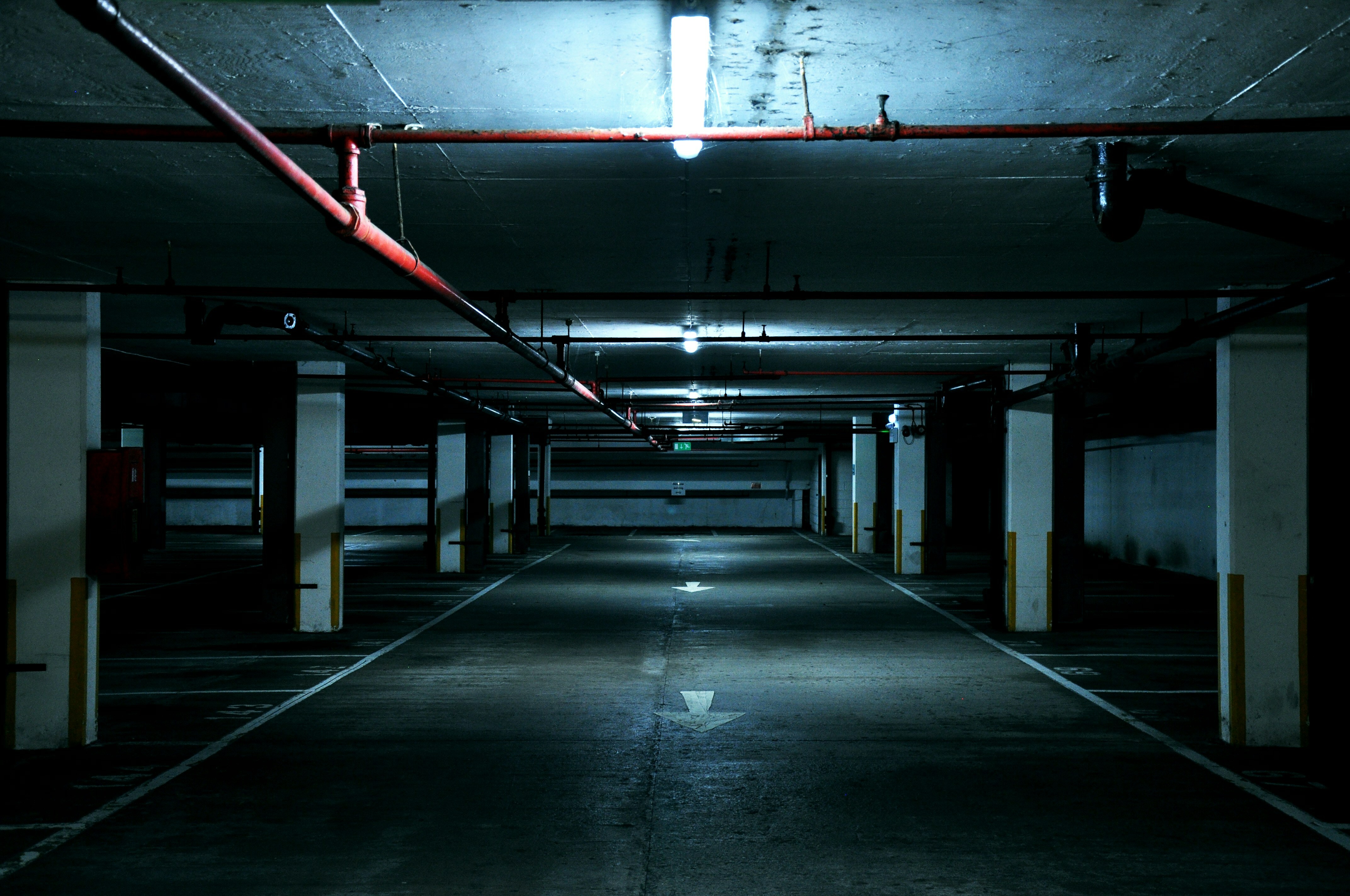 Dimly lit underground carpark, long winding corridor with concrete walls, floor, and pipes above.