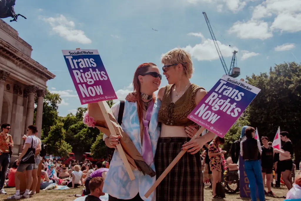 Two people holding "Trans Rights Now" signs at an outdoor protest.