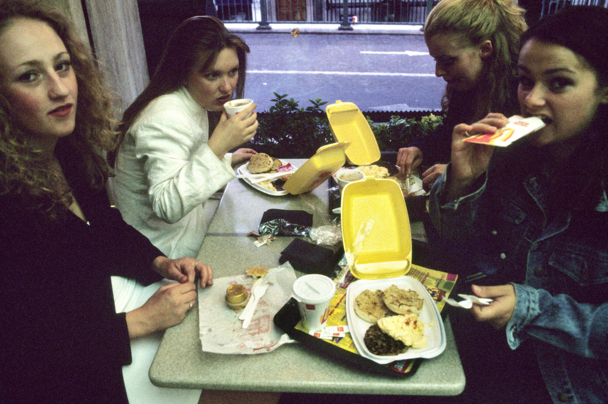 Four young women eating lunch at a table, with trays of food and drinks in front of them.