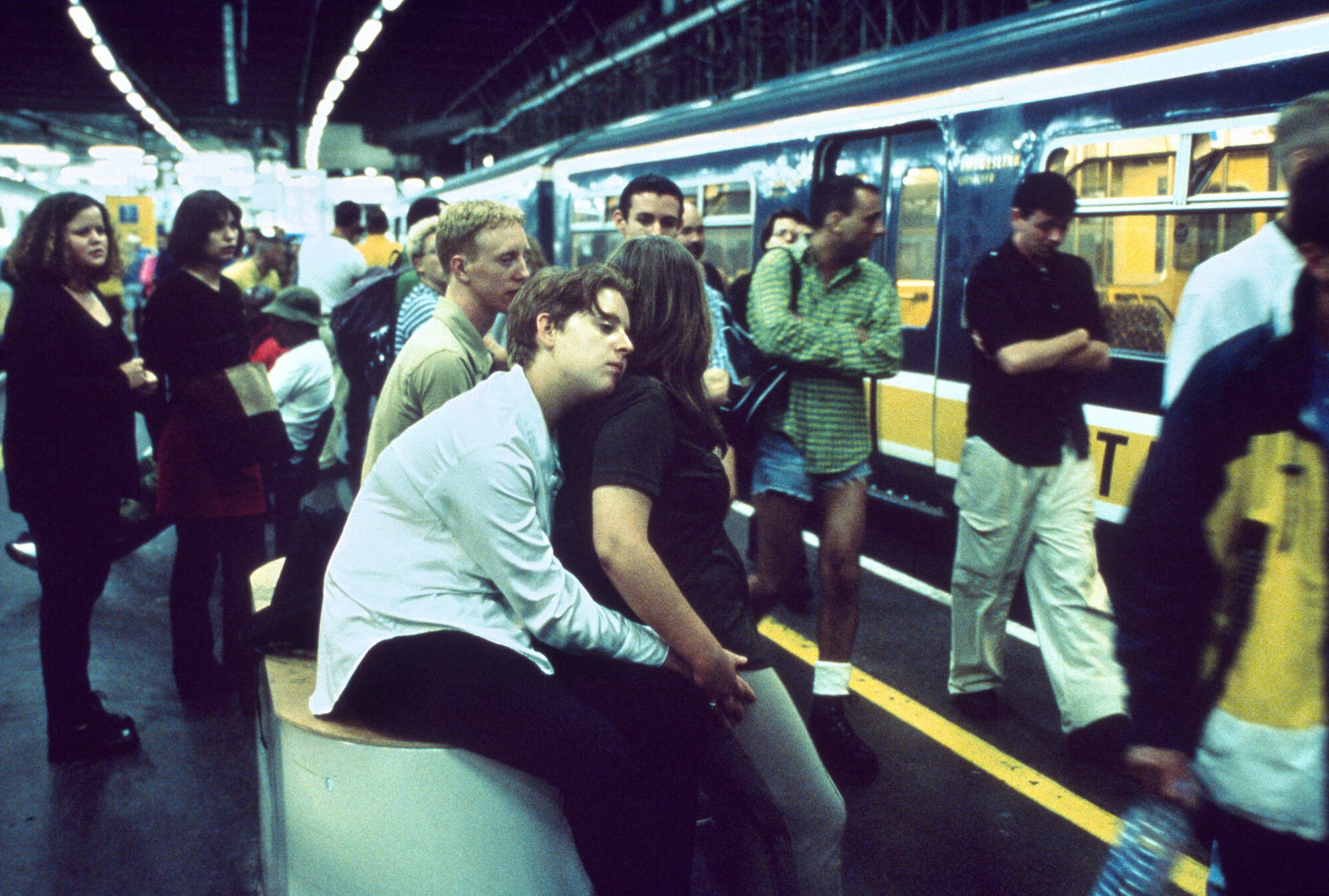 Crowded interior of a commuter train, passengers standing and sitting.