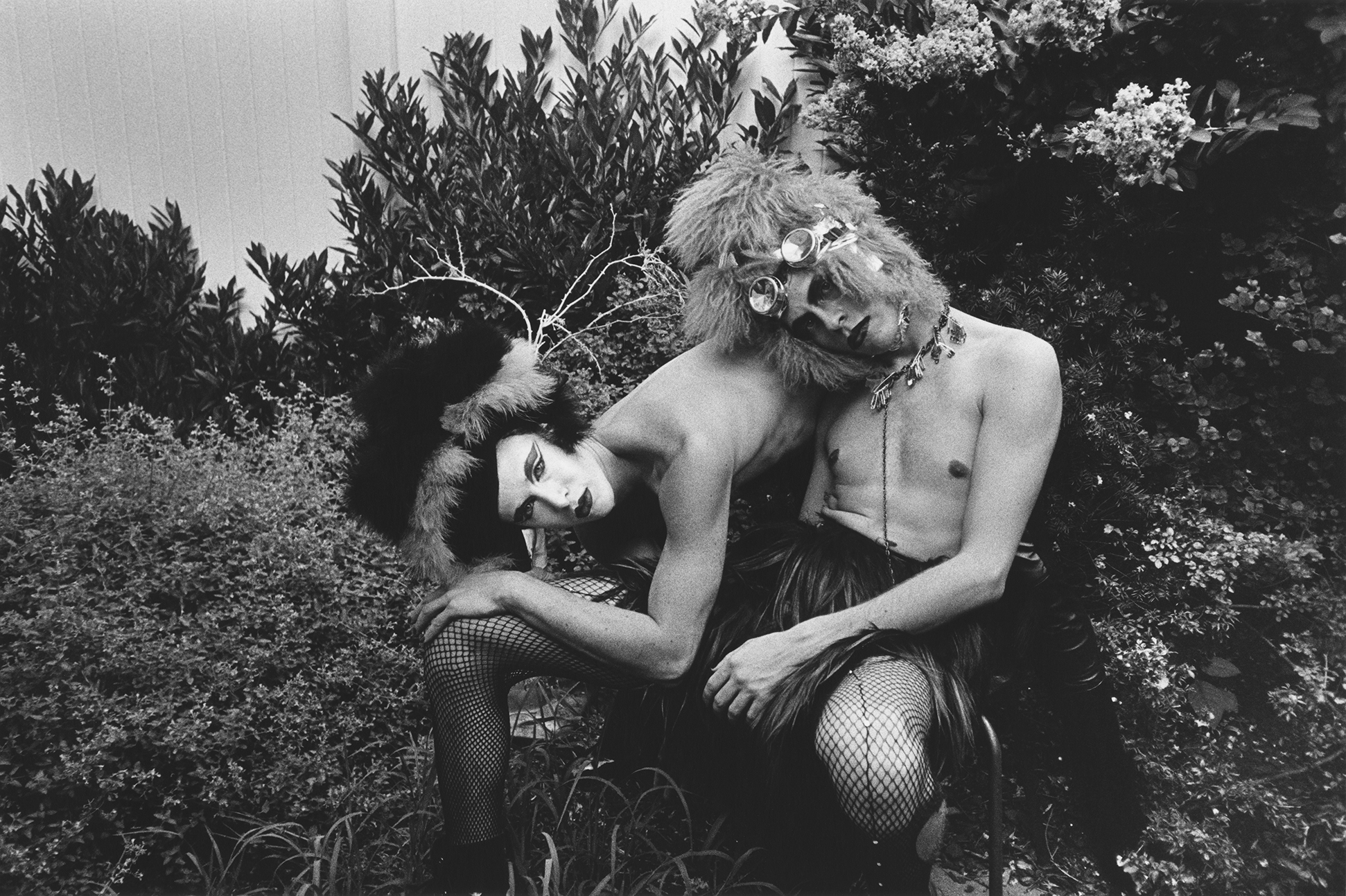 Monochrome image of two nude figures embracing amid foliage.