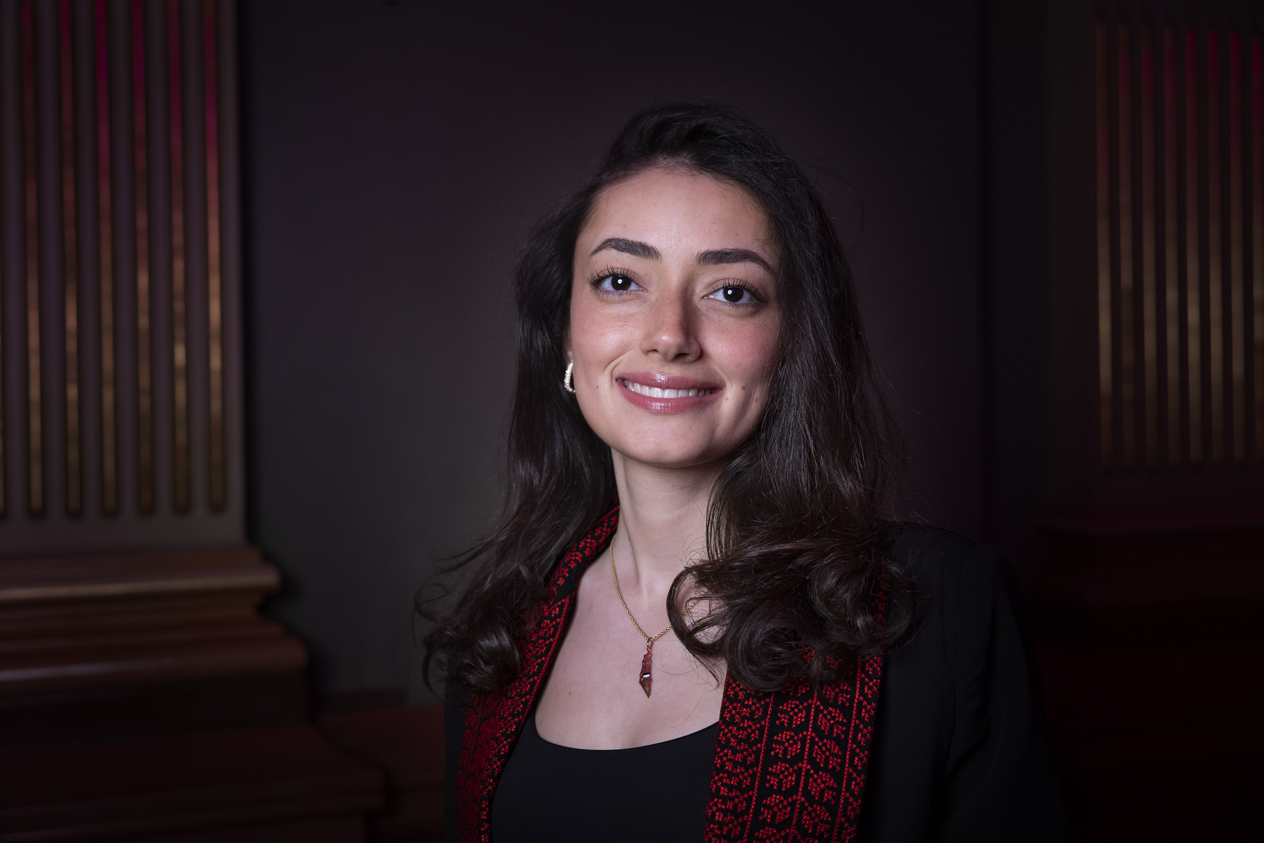 A woman with dark, curly hair and a red cardigan, smiling at the camera.