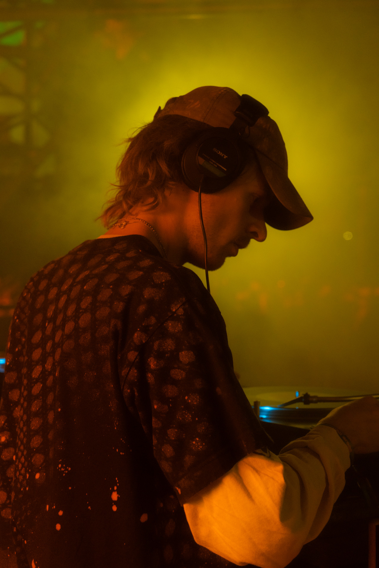 A person wearing a baseball cap and a patterned jacket, silhouetted against a yellow and orange background.