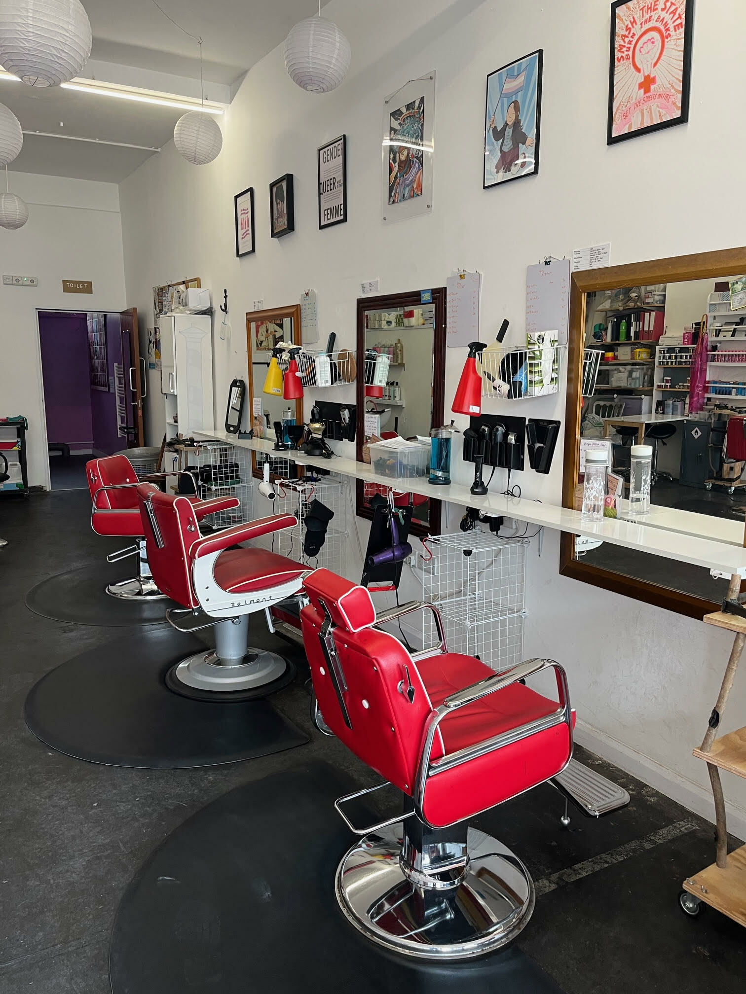 Interior of a retro-styled hairdressing salon. Bright red leather styling chairs, mirrored vanities, and framed posters on the walls create a vintage aesthetic.