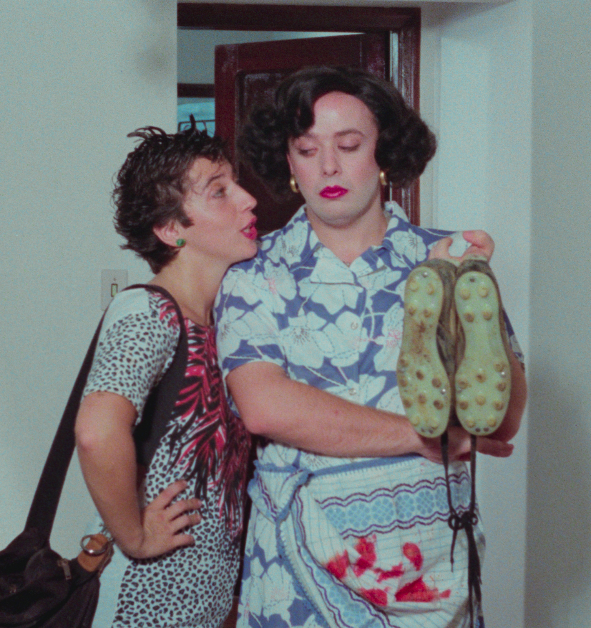 Two women wearing colourful, patterned clothing standing together in a room.