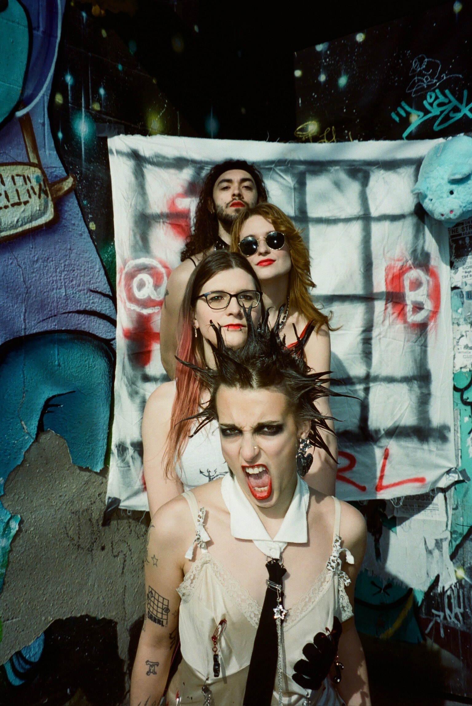 Three young women posing together in front of a graffiti-covered wall, wearing stylish outfits and accessories.