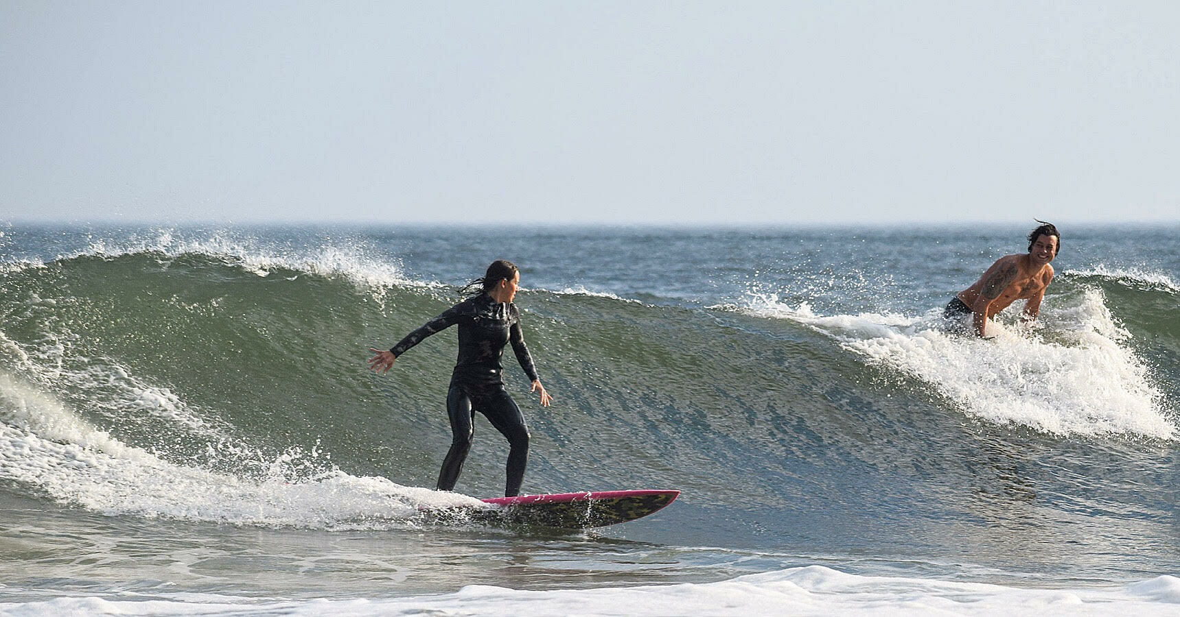 Two surfers riding waves in the ocean, with spray and ocean in the background.