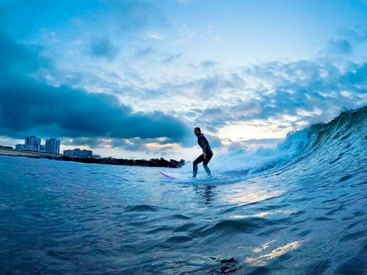Surfer riding large crashing wave against cloudy sky in the distance.