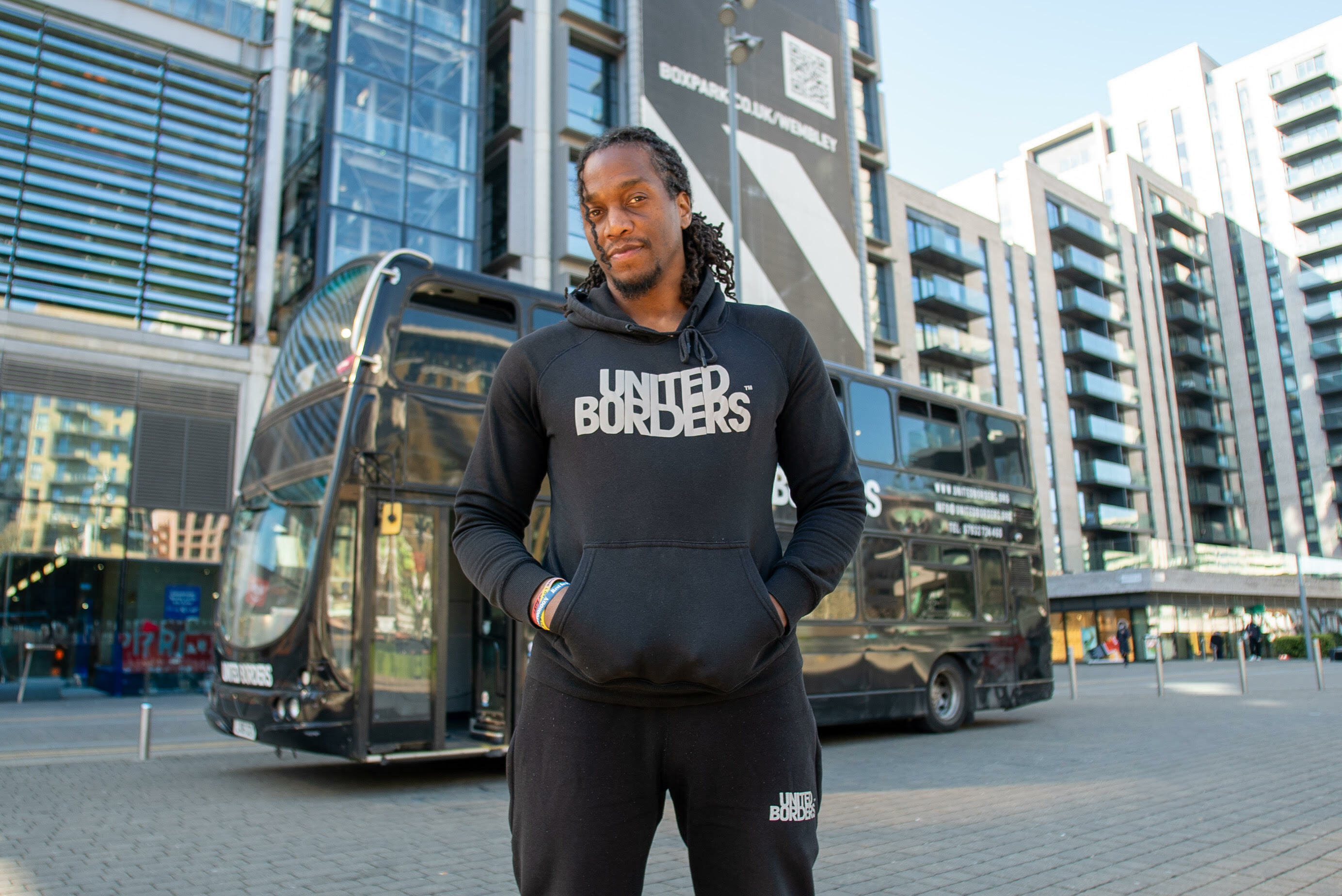 A person wearing a black hoodie with the text "United Burgers" standing in a city street with tall buildings in the background.