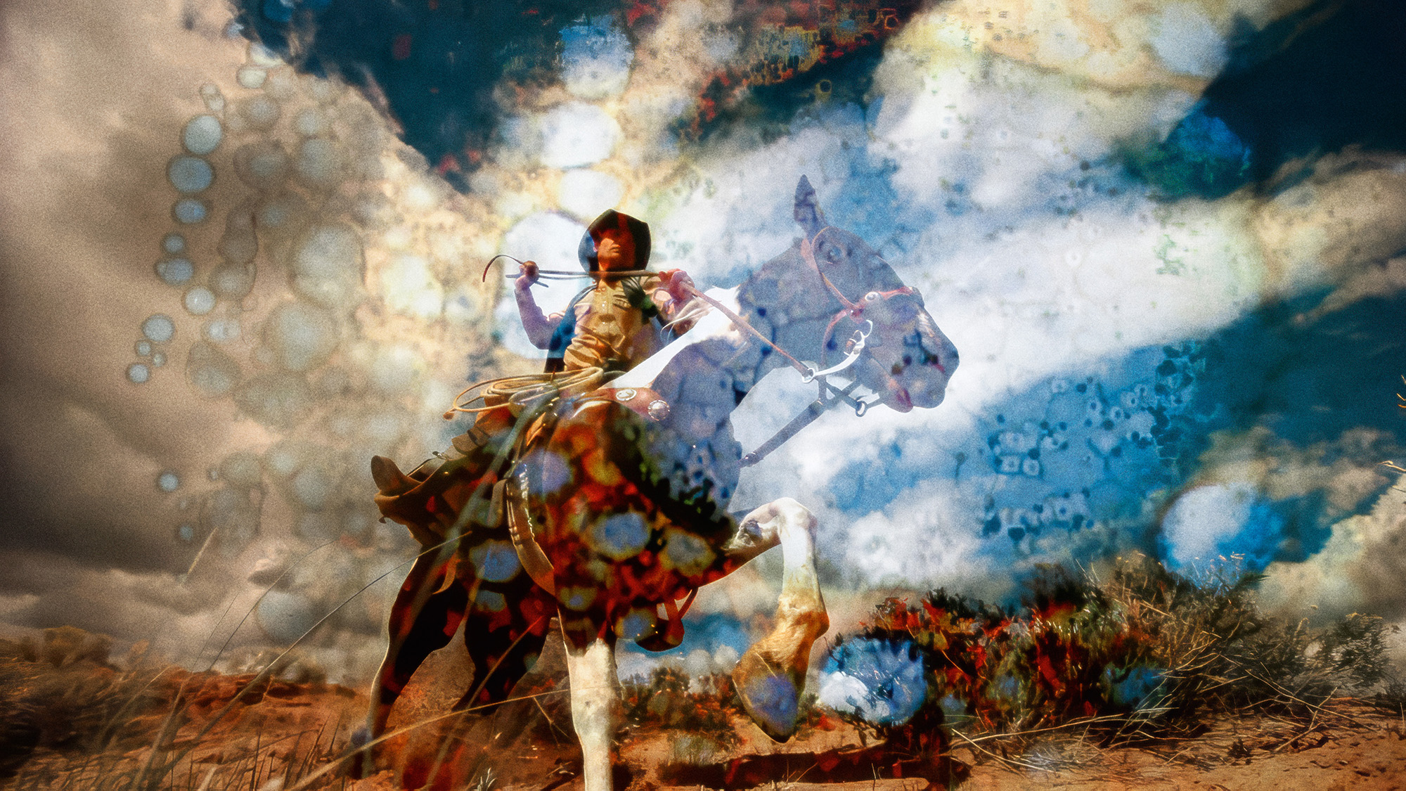 Figure on horseback with raised sword against dramatic cloudy sky. Brown and white horse, desert landscape with warm earth tones and blue-white clouds.