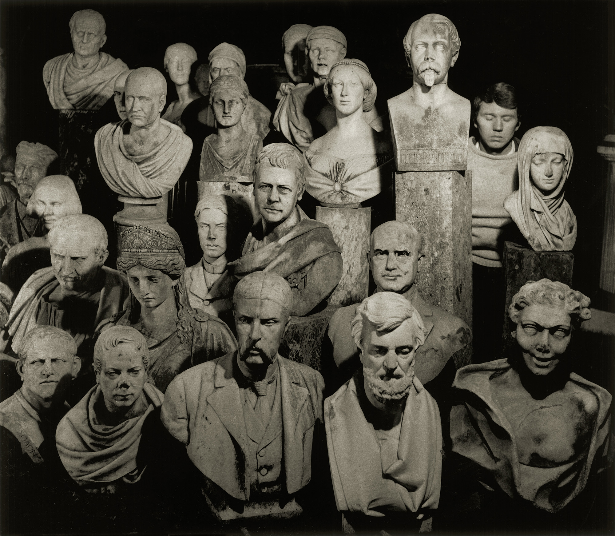 Collection of marble and plaster busts arranged in rows against black background, featuring various classical and period portrait sculptures.