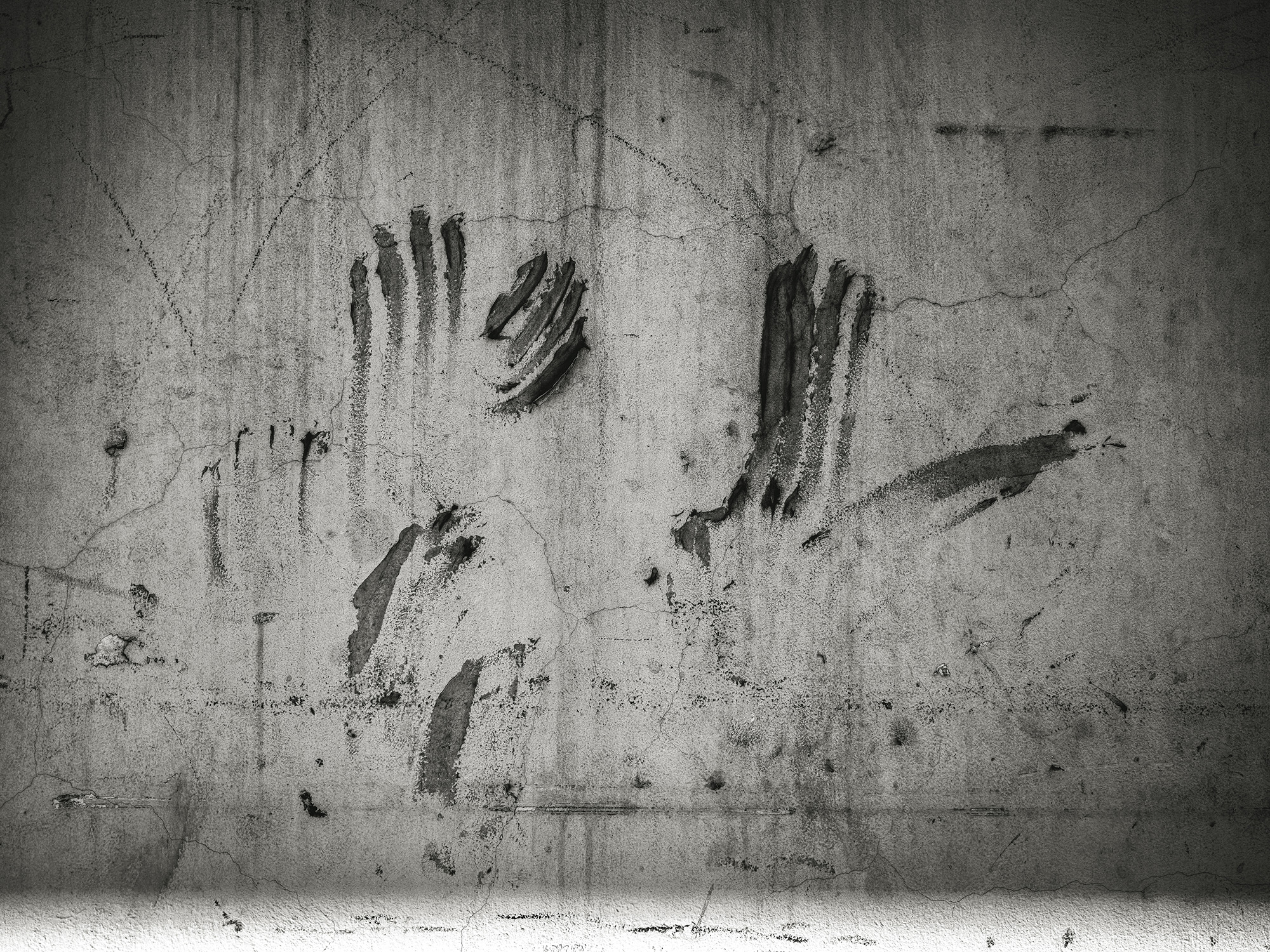 Dark handprints pressed against weathered grey concrete wall with vertical staining and surface cracks.