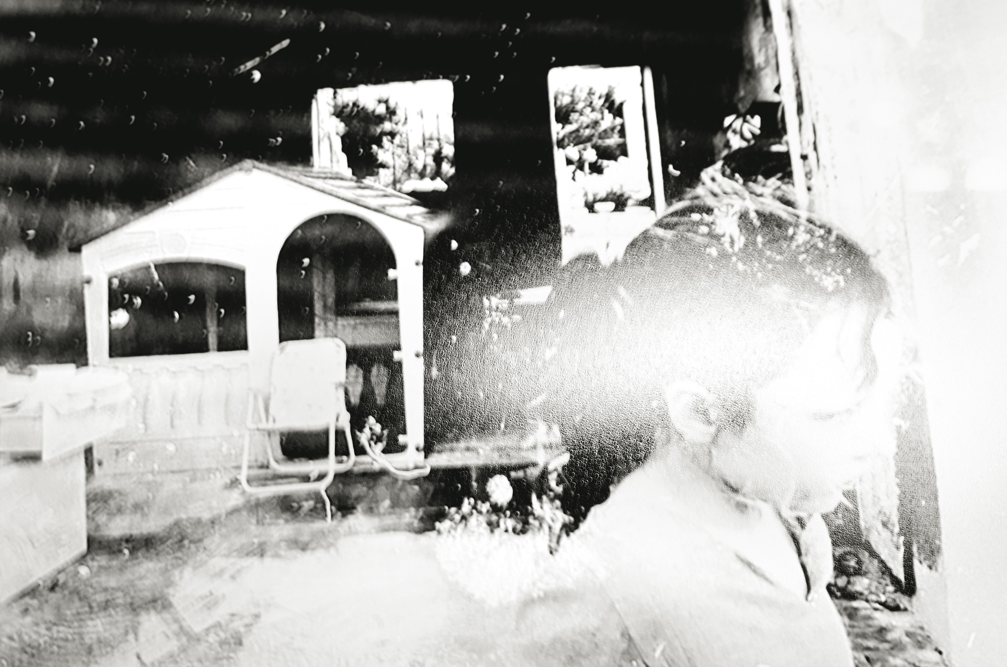 Black and white image showing snow-covered railway locomotive with white house structure in background, heavy snow accumulation throughout scene.