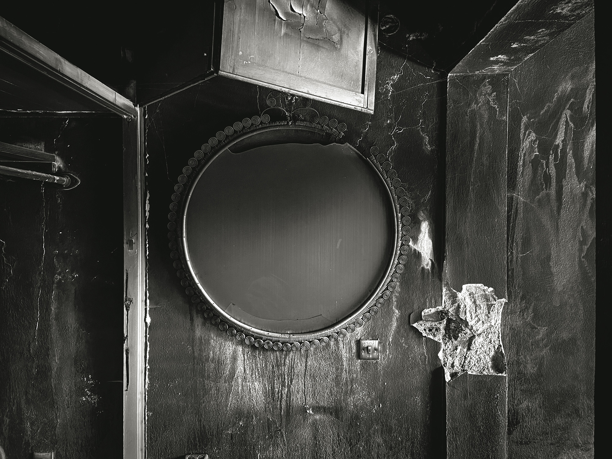 Fire-damaged bathroom with blackened walls, round mirror, white toilet, and charred surfaces throughout small space.