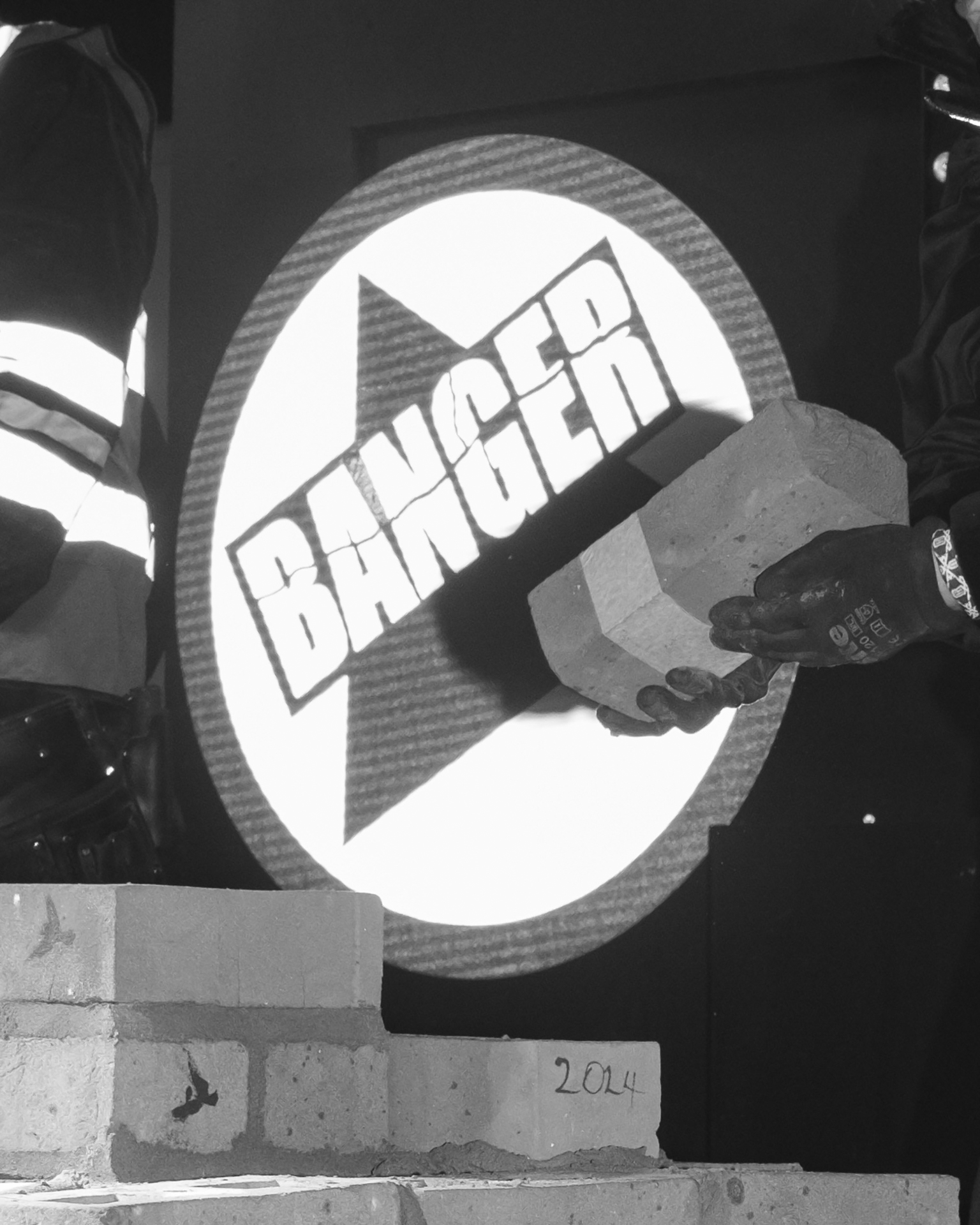 Black and white image showing circular sign with "BANGER" text in bold letters across diagonal banner shape in centre.