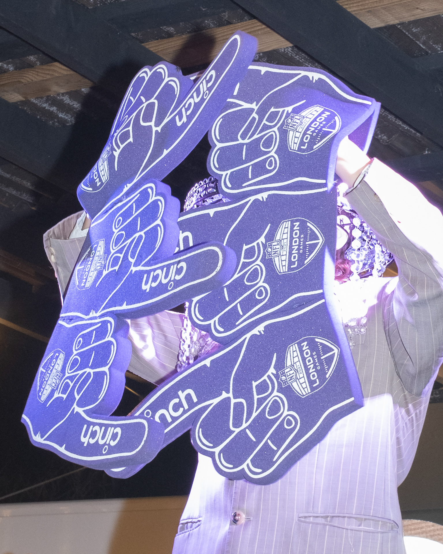 Person wearing white shirt holds multiple purple foam hands with "UofR" text and finger pointing gestures in clear plastic bag.