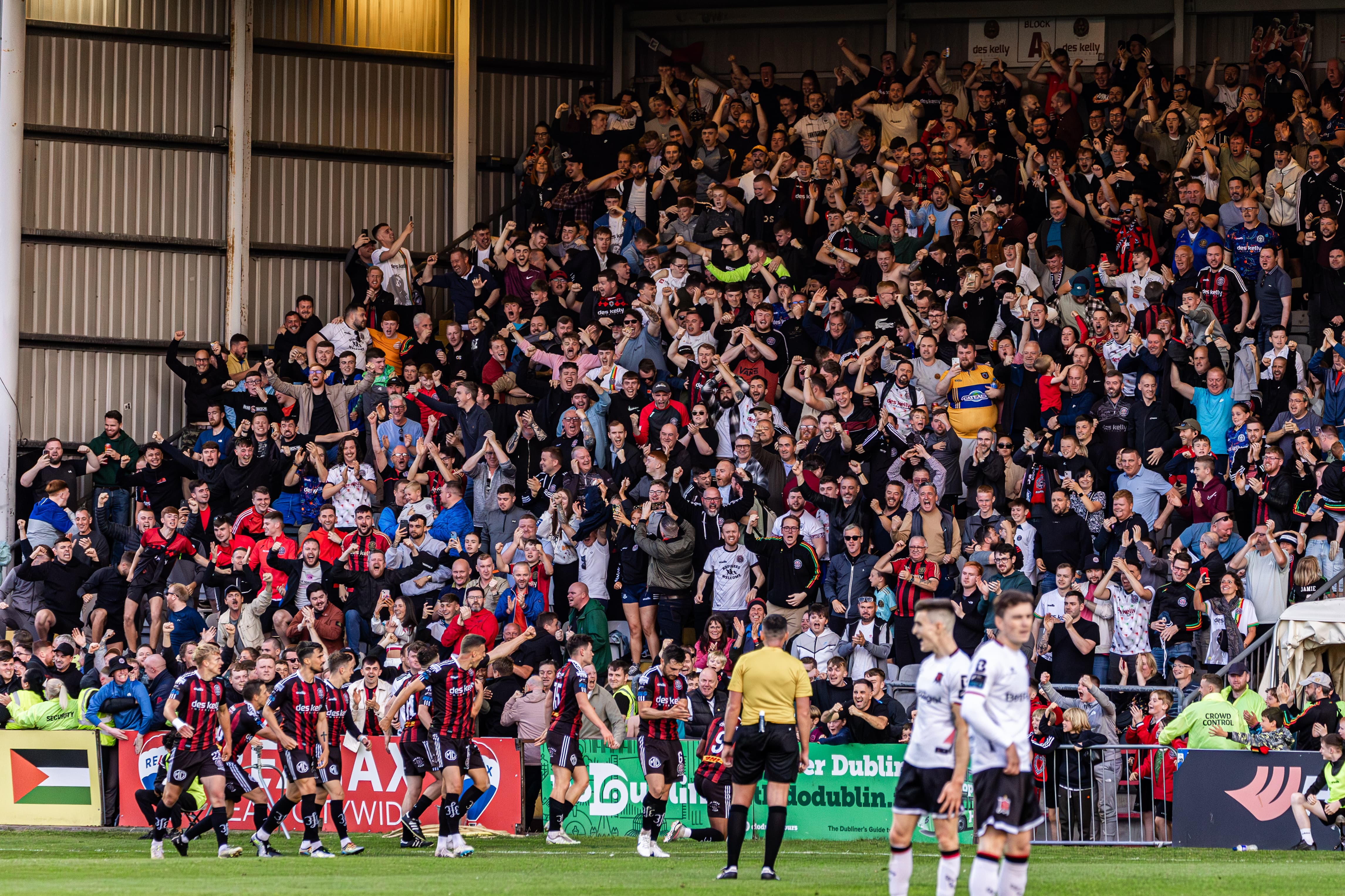 Large crowd of football fans in stadium stands, cheering and waving.