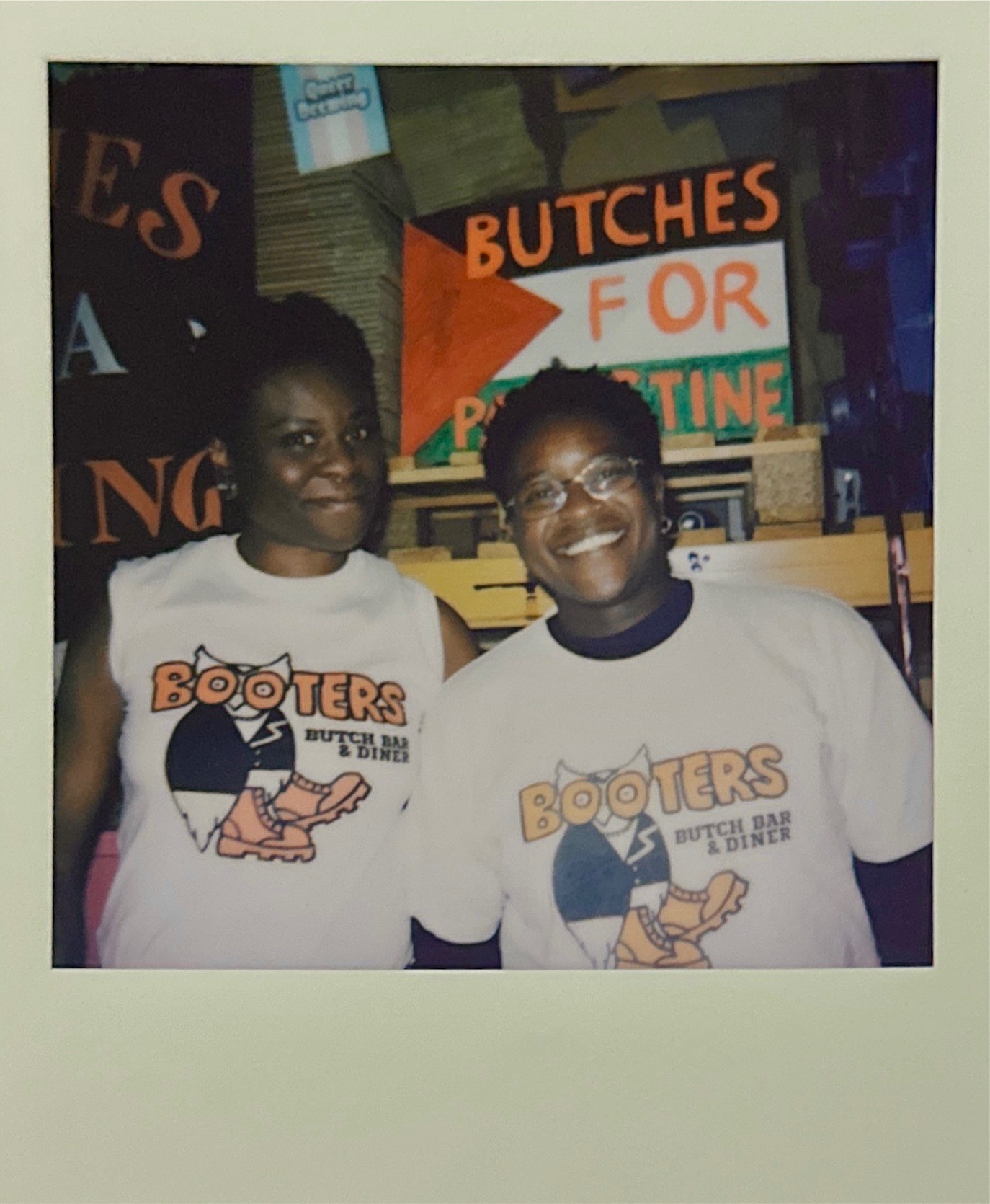 Two people wearing matching white Hooters t-shirts standing together indoors, with orange and white signs visible in background.