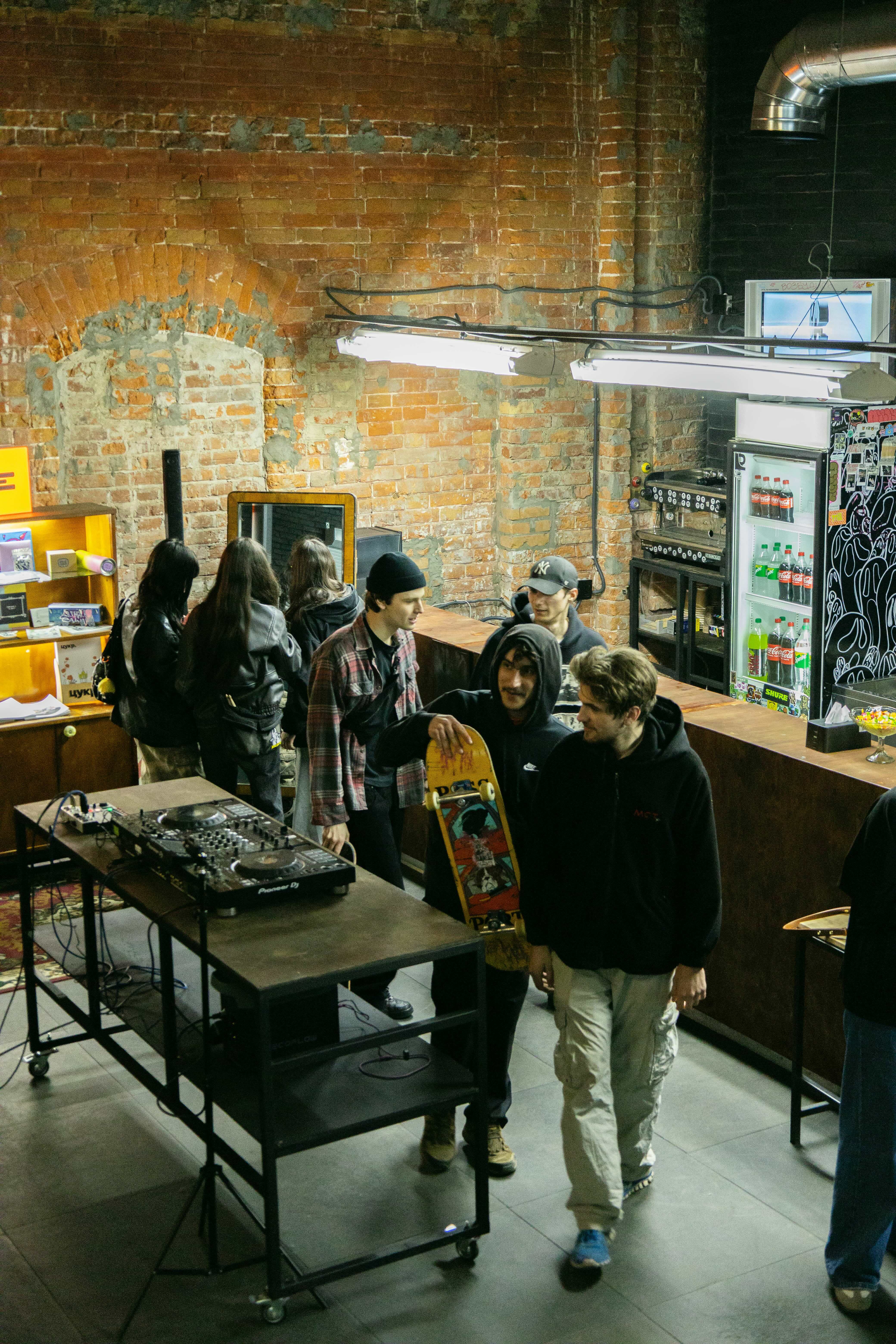 Group of people in a workshop setting with brick walls, equipment, and shelves.
