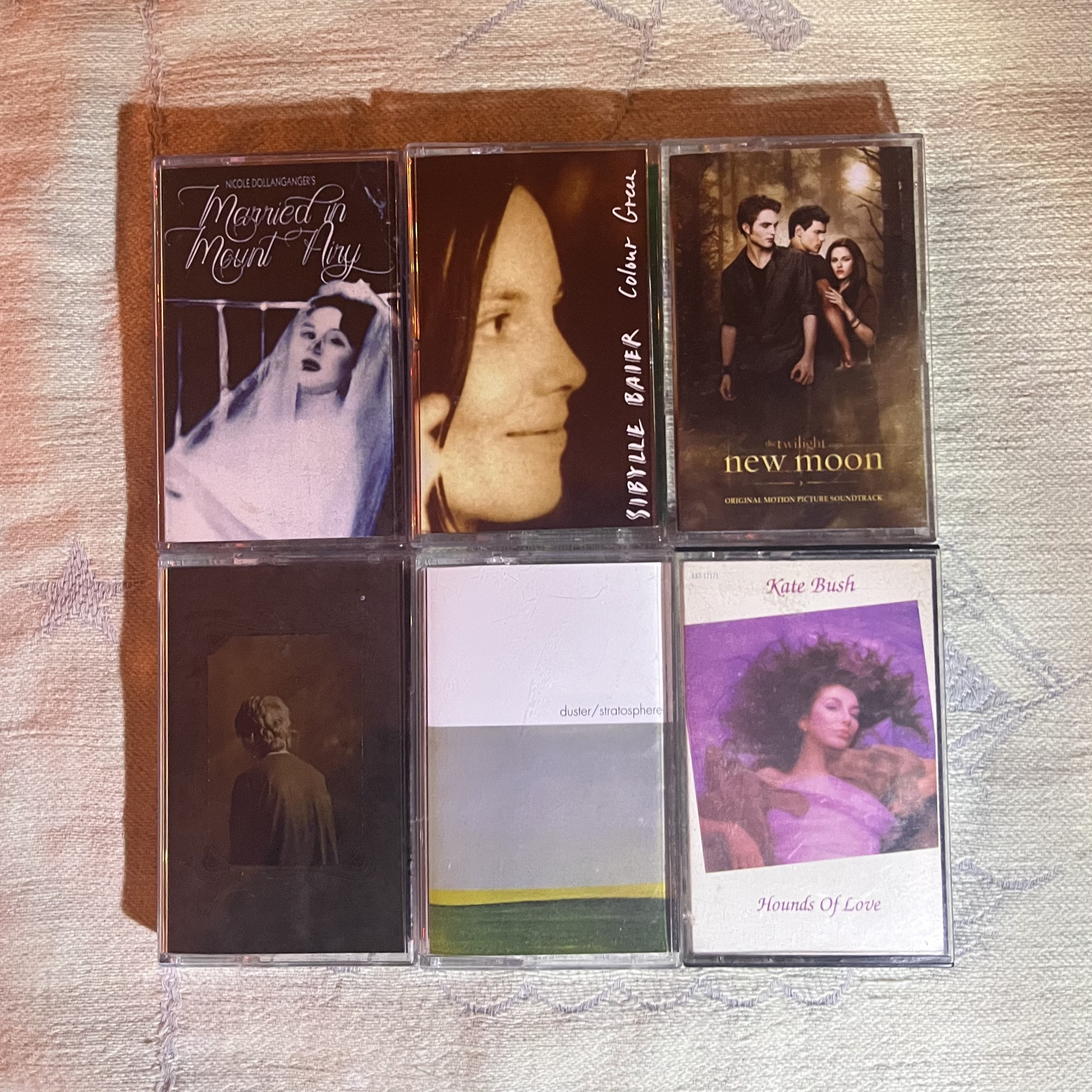 Six cassette tapes arranged in two rows on wooden surface, including Marilyn Manson, Twilight New Moon soundtrack, and Kate Bush albums.