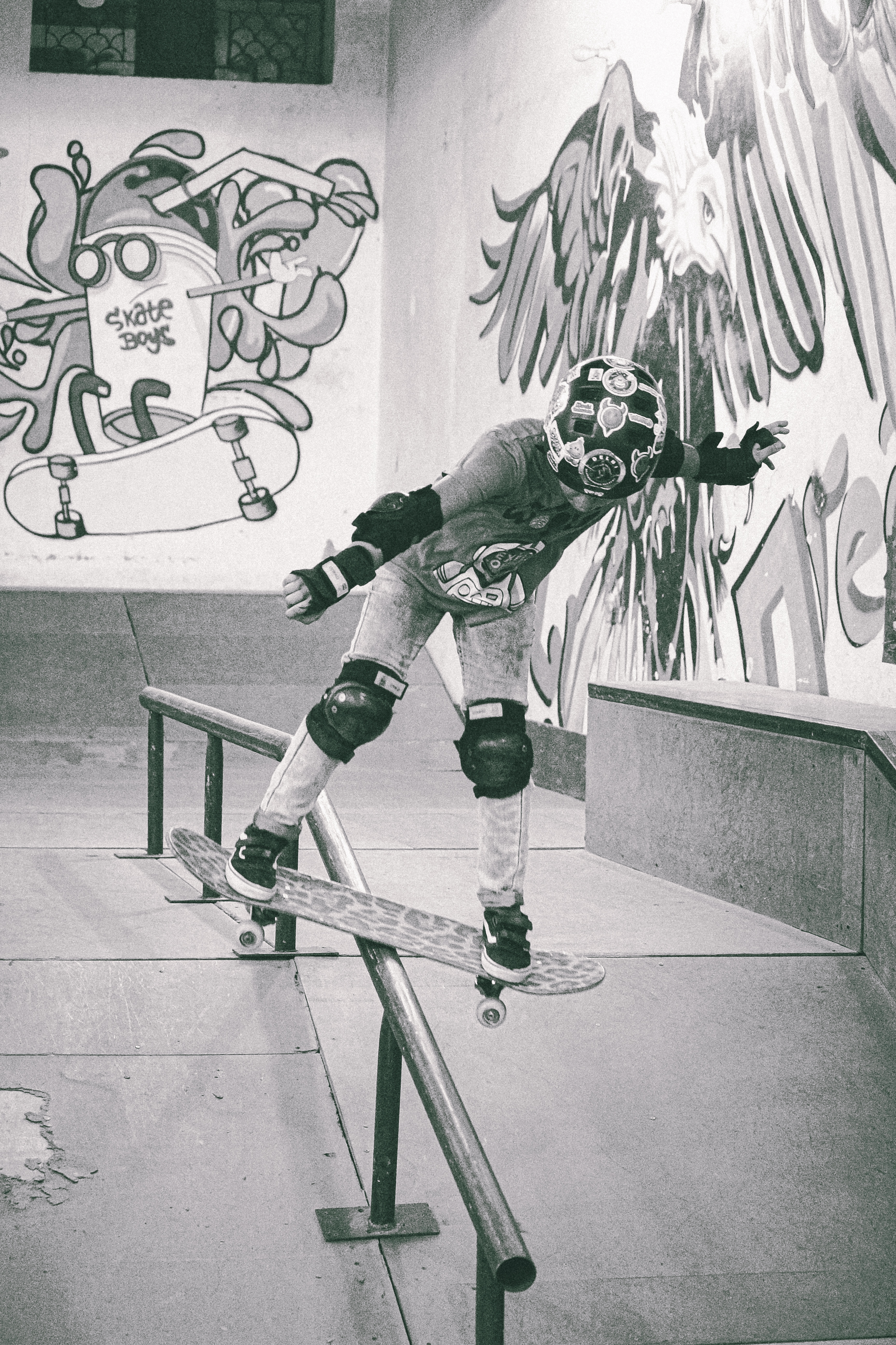 Skateboarder wearing gas mask and protective gear grinding on rail at indoor skate park with graffiti-covered walls