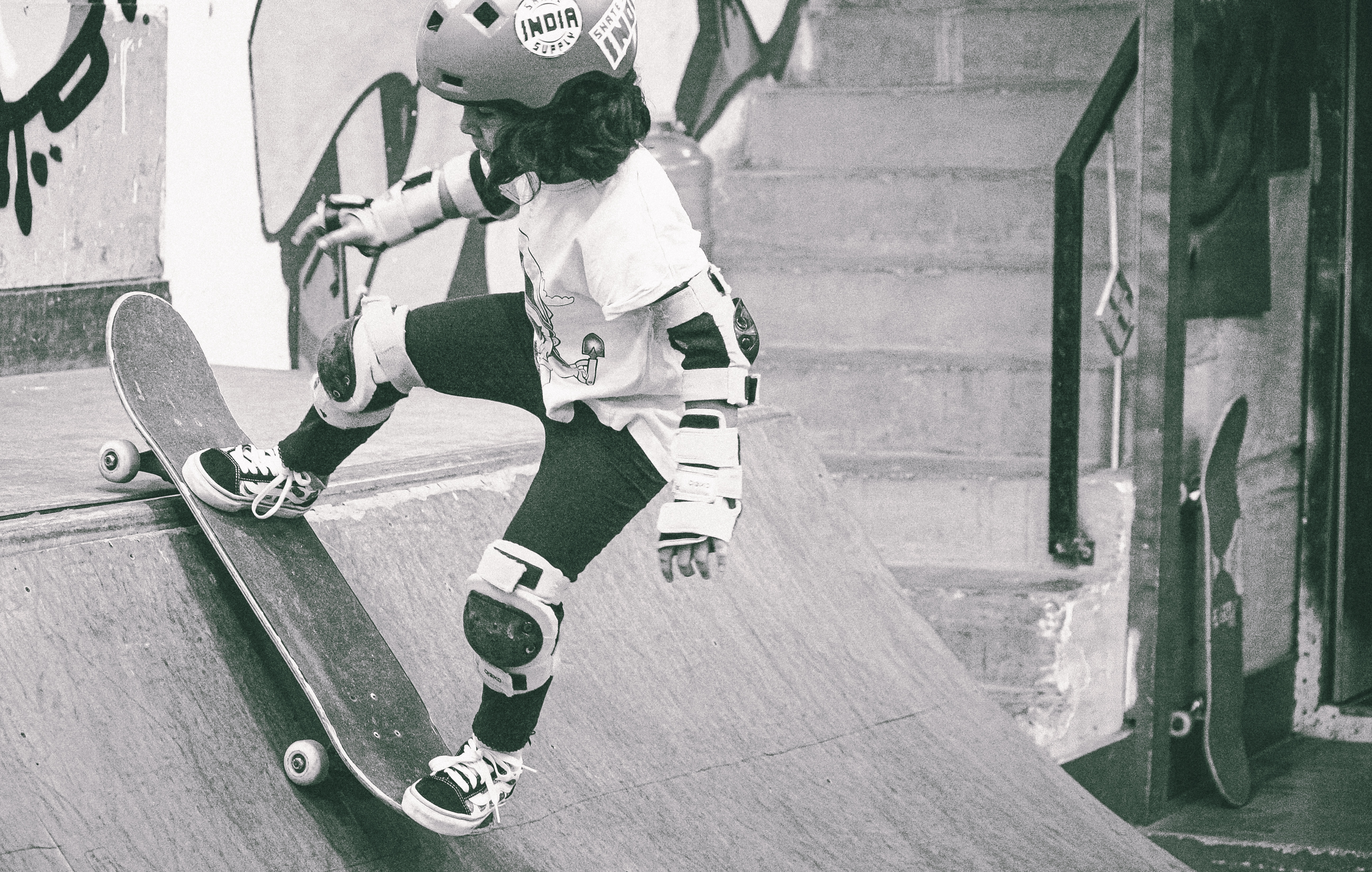 Black and white image showing skateboarders' legs and boards on concrete steps, with white protective gear and dark shadows.