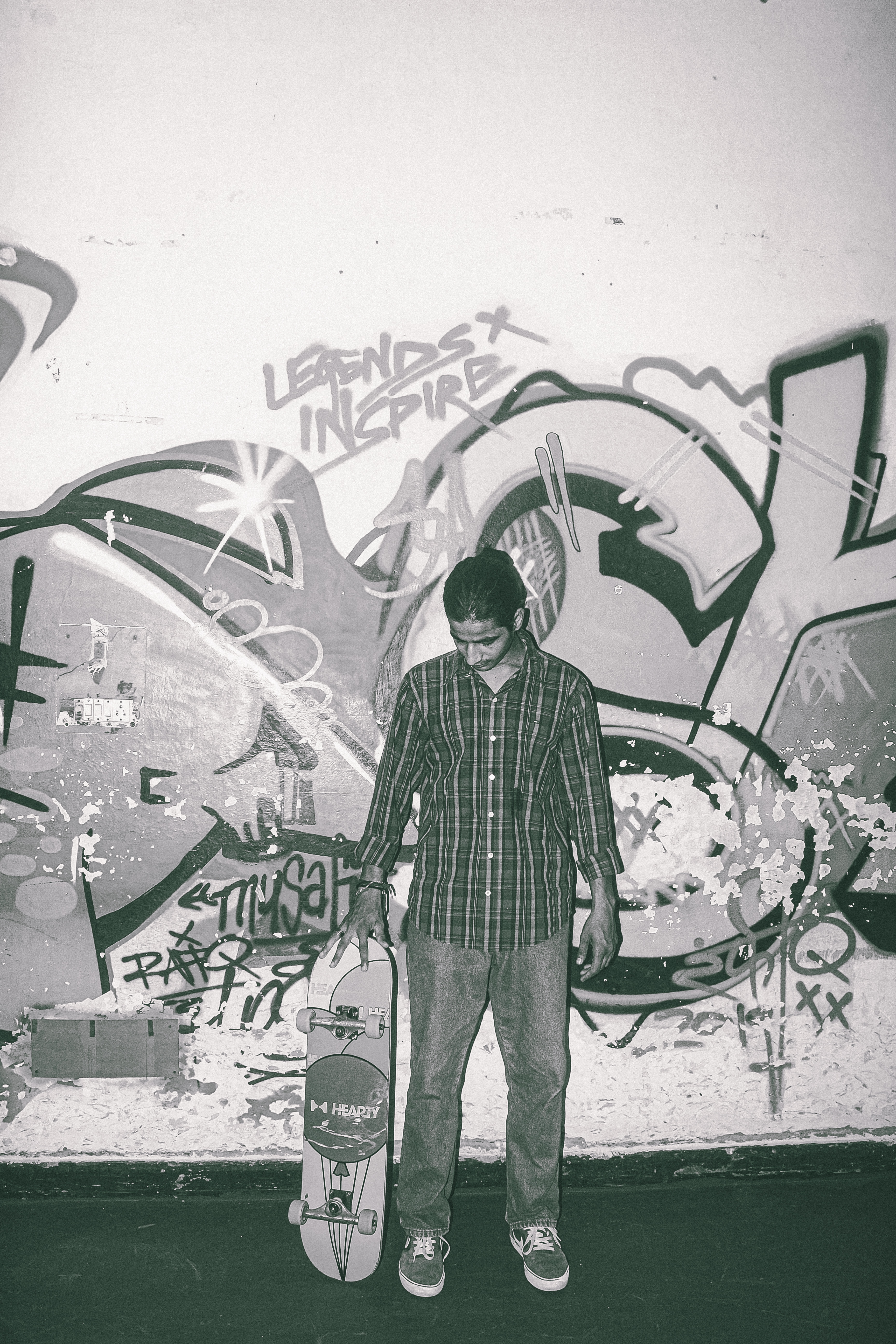 Man in plaid shirt holding skateboard standing against wall covered in colourful graffiti and street art.