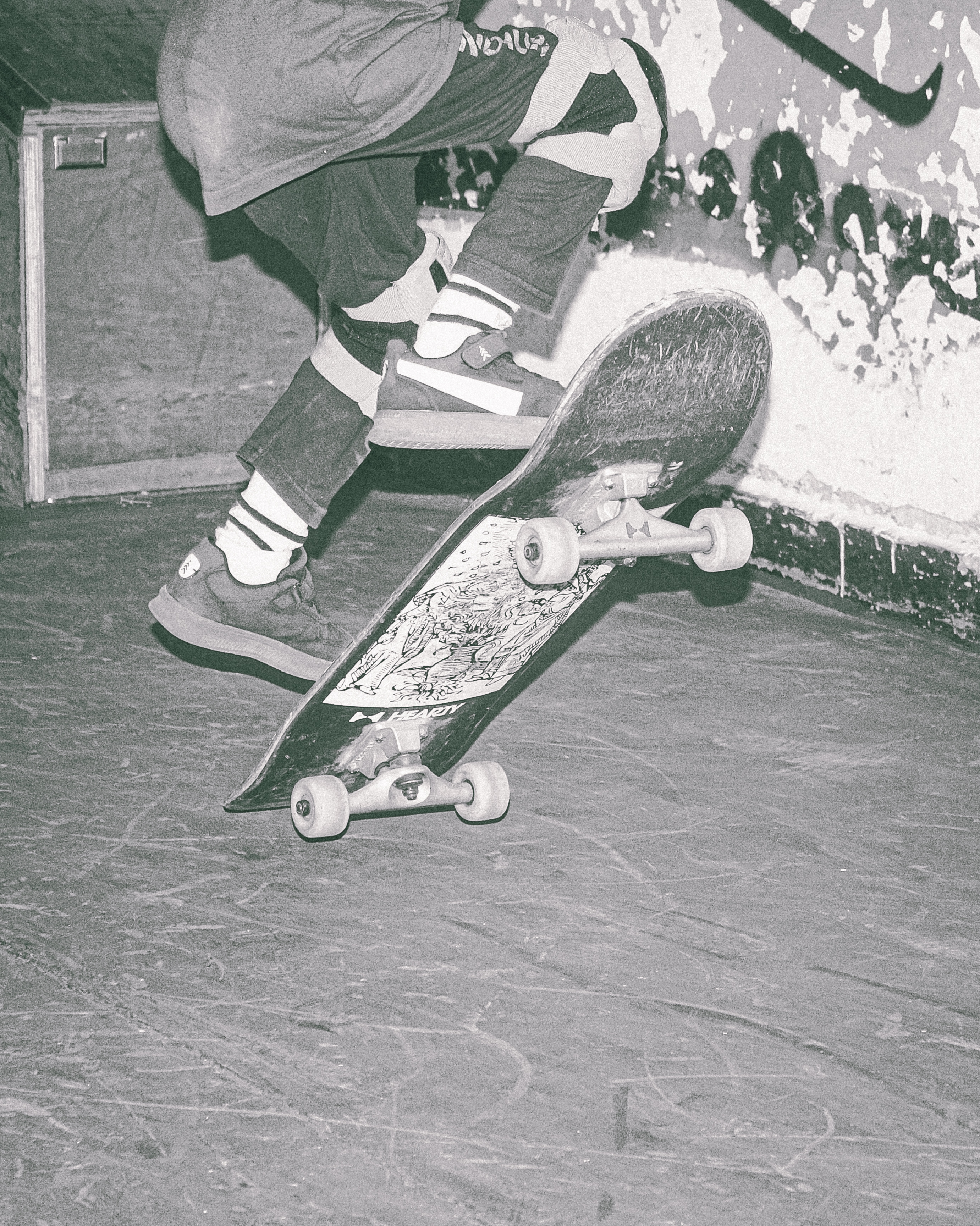 Person skateboarding in concrete bowl, wearing striped socks and trainers, skateboard visible mid-air, black and white photograph.