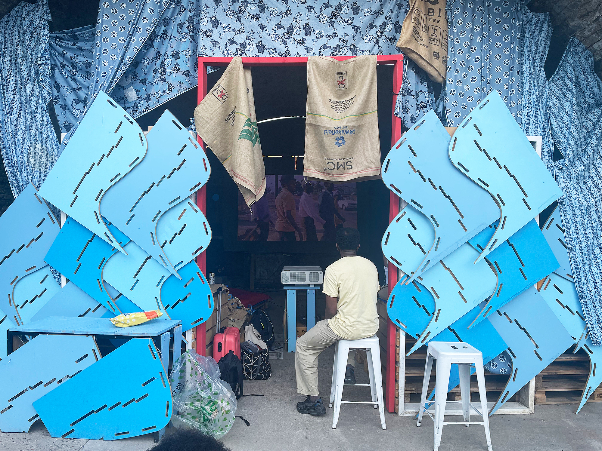 Assorted fabric, chairs, and stool in a market stall; blue and red elements create a visually striking composition.