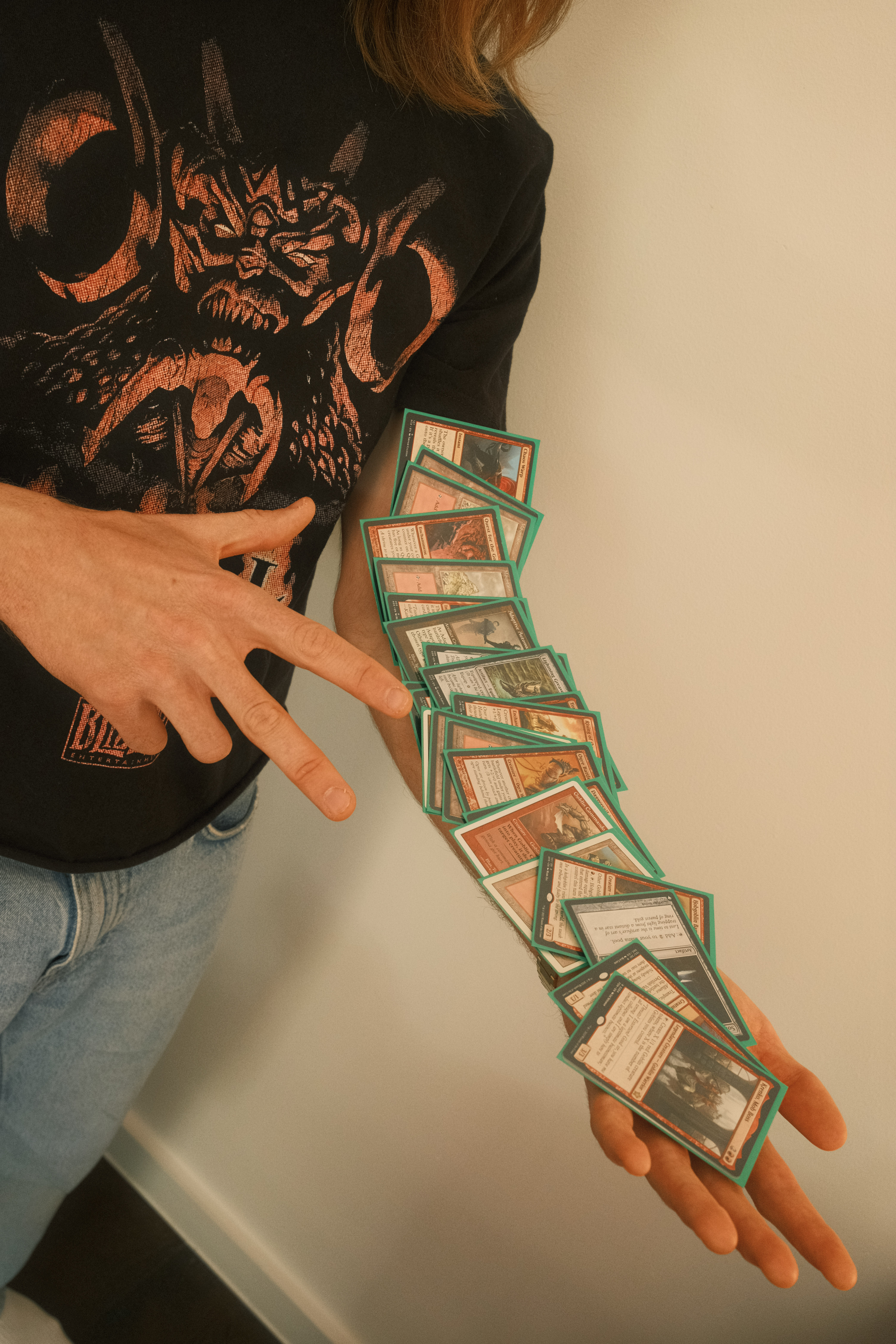 Person in black shirt with orange dragon design holds fanned trading cards with green borders between outstretched hands.