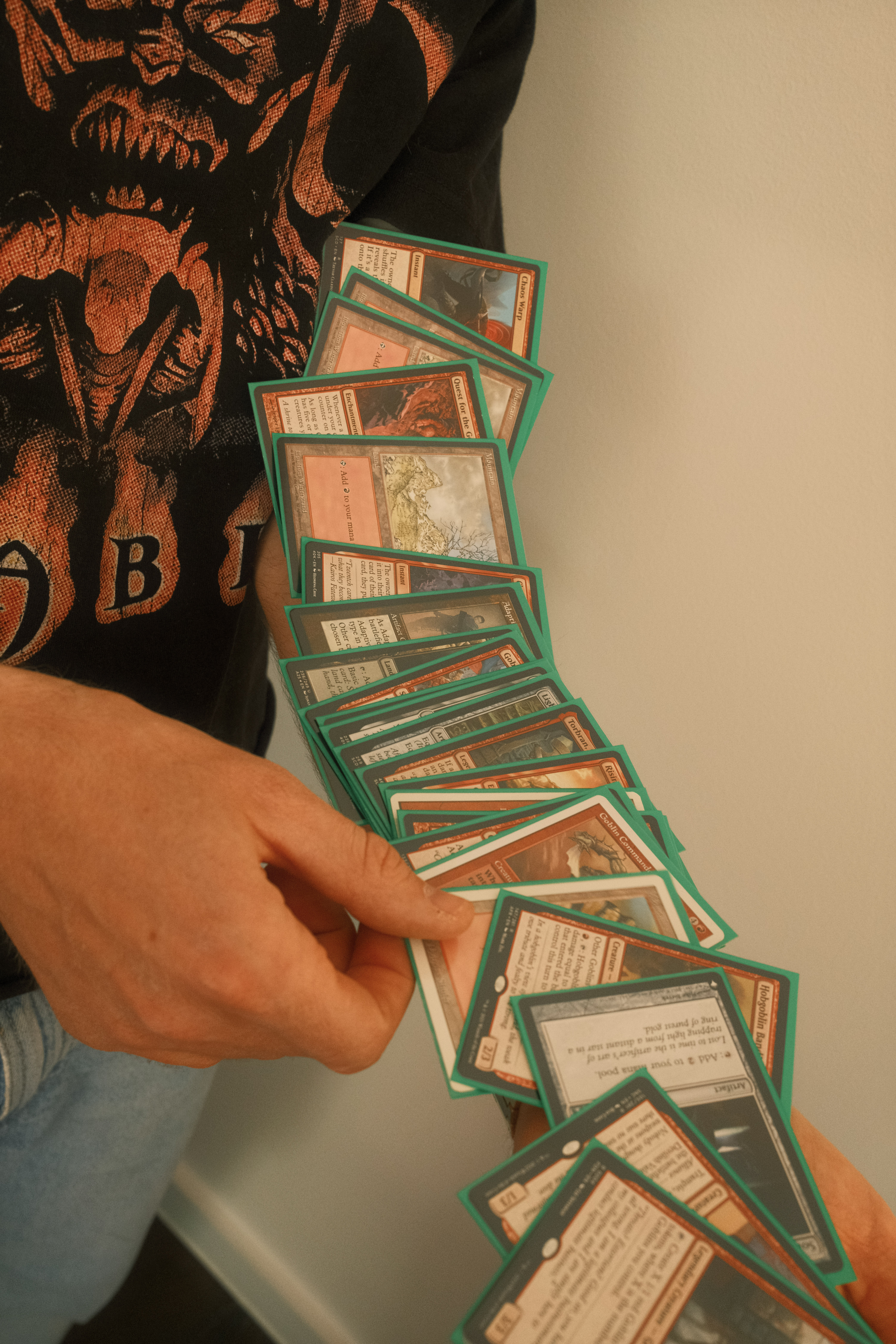 Person in black t-shirt holding fanned-out green-bordered trading cards, displaying them in an arc formation against white background.