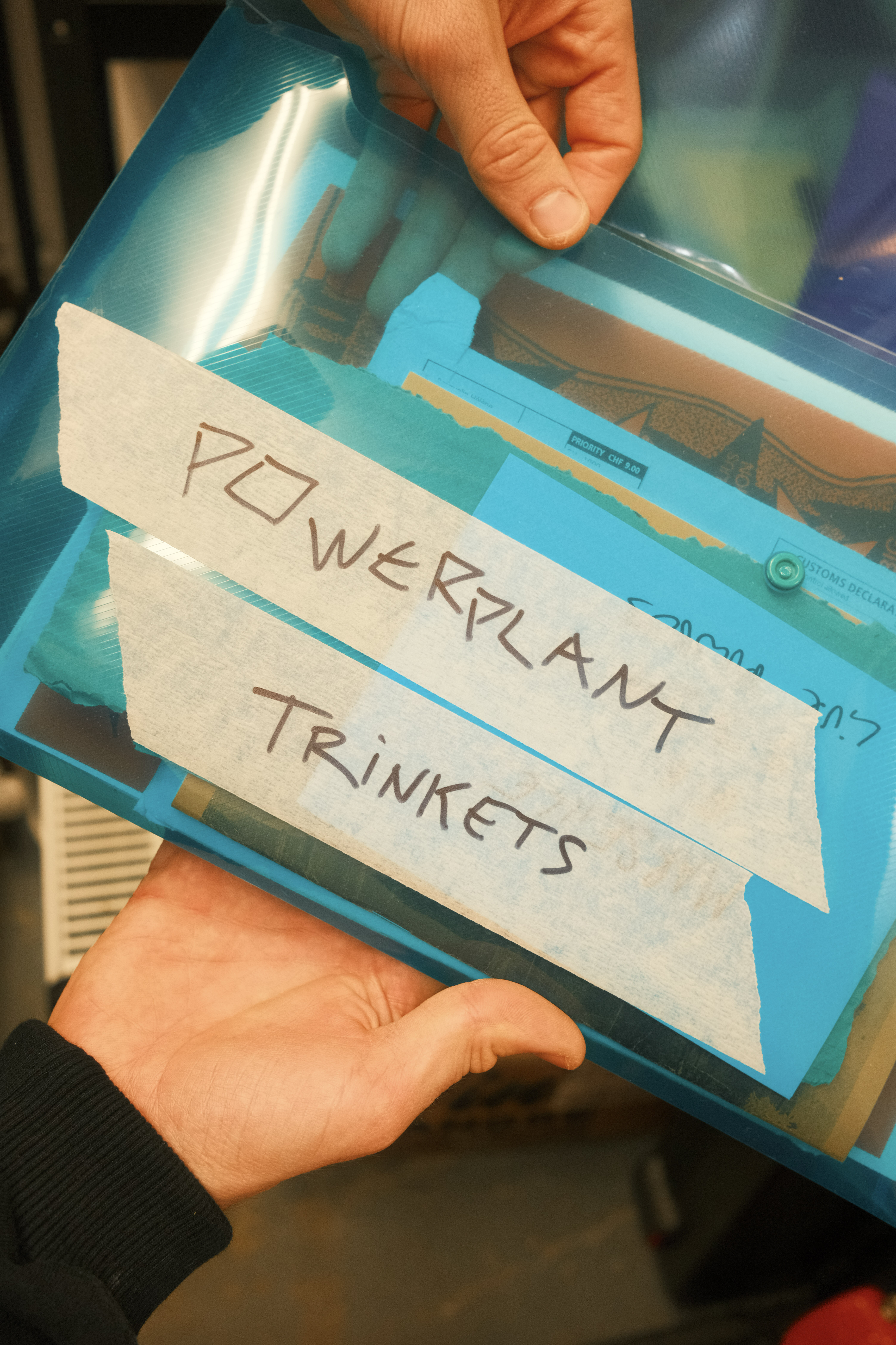 Hands holding teal plastic container with white label reading "POWERPLANT TRINKETS" in black text.