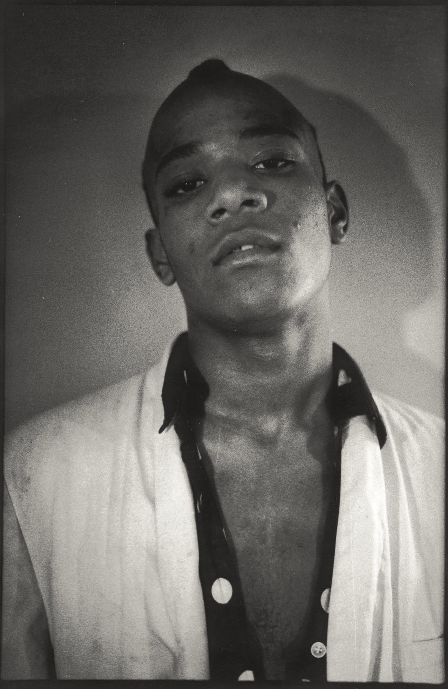 Black and white portrait of a young Black man looking upward, wearing an unbuttoned white shirt over a dark shirt.