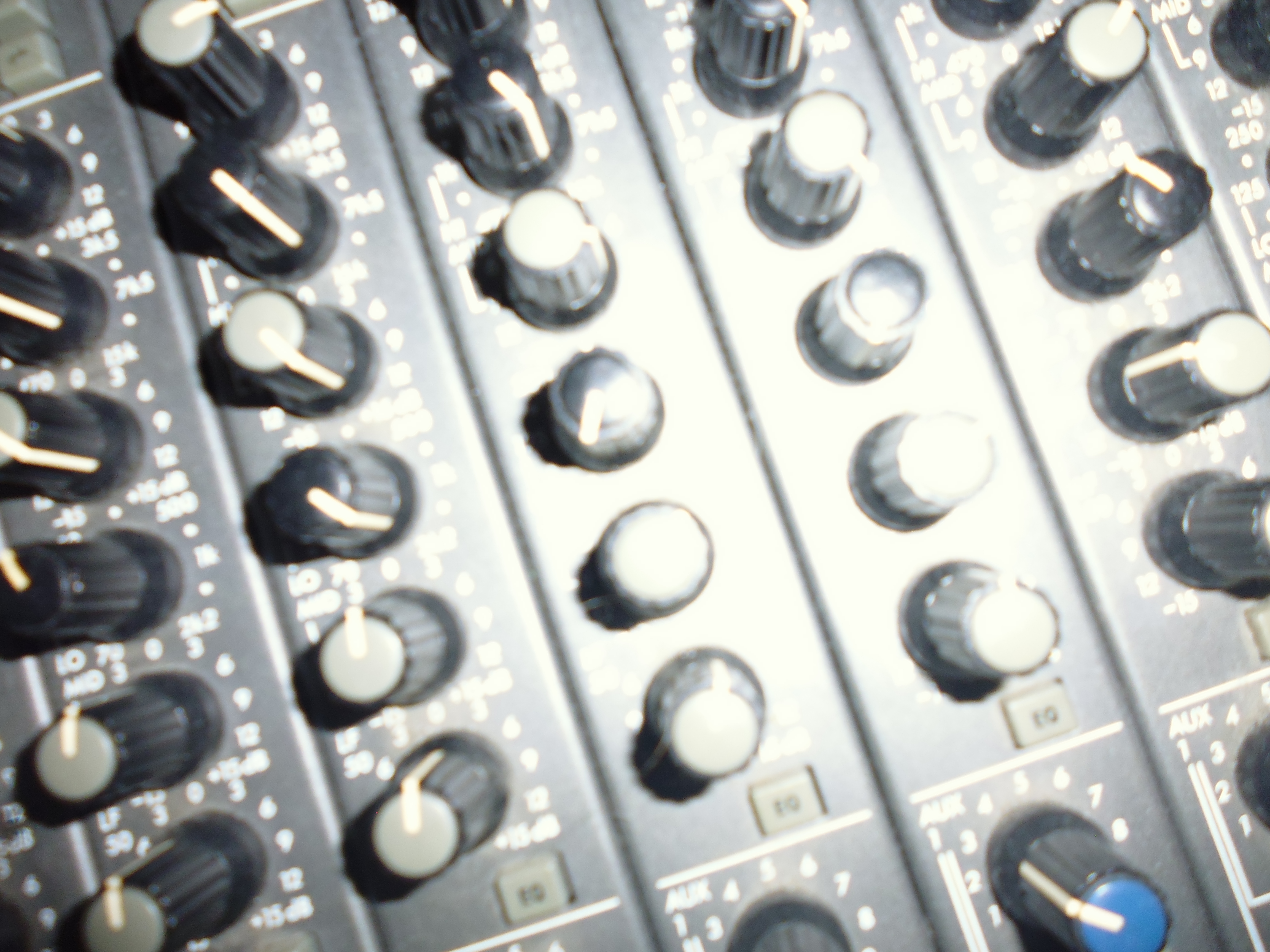 Close-up of silver audio mixing console with multiple rows of black rotary knobs and white control panels with printed text.